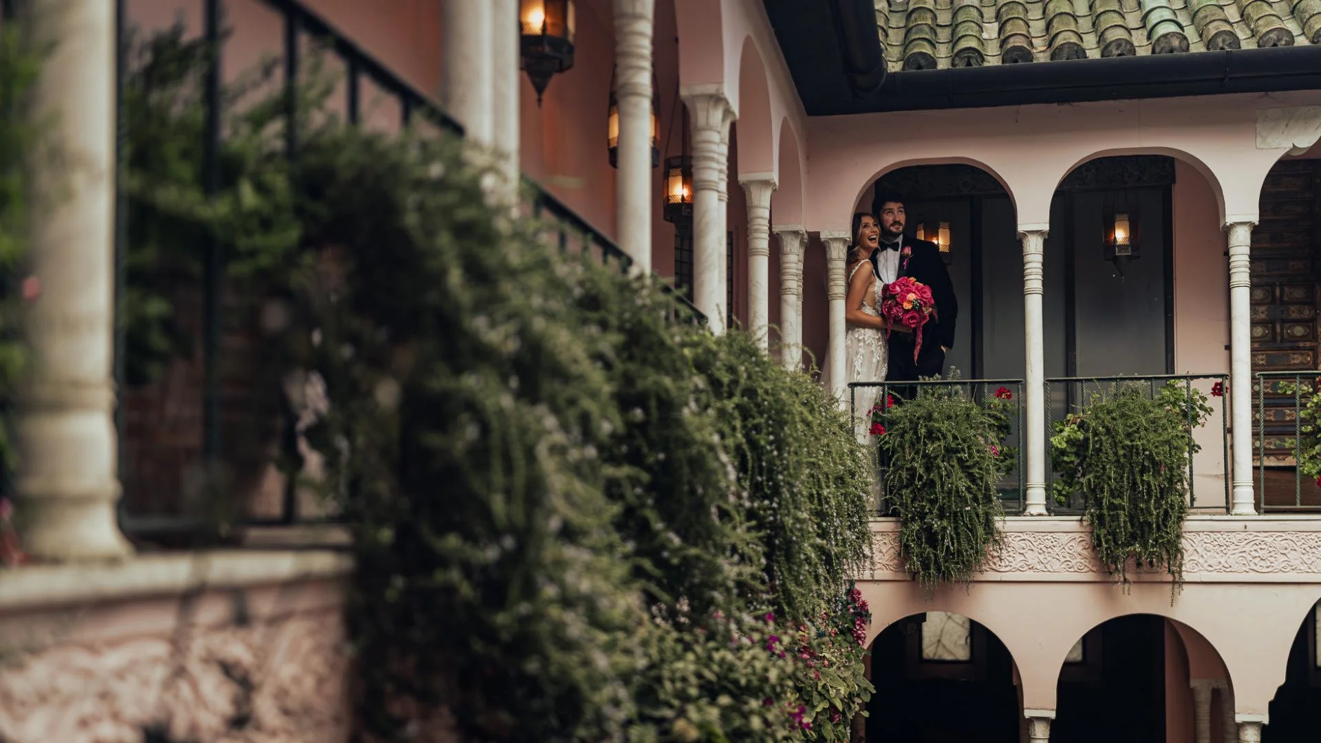 A couple laugh together in a courtyard full of archways during their black-tie destination wedding.