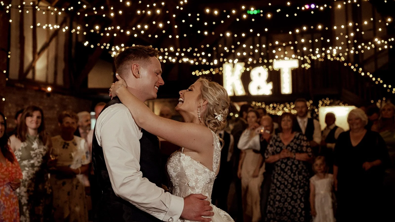 A couple laugh as they share their first dance in the Tithe Barn at Cooling Castle Barn, Kent.