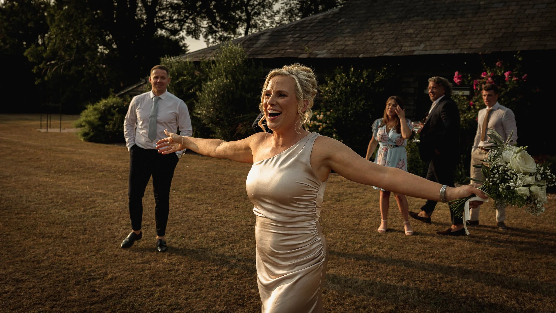 A candid wedding moment shows a bridesmaid celebrating with her arms outstretched, captured during golden hour portraits at Winters Barns in Kent.