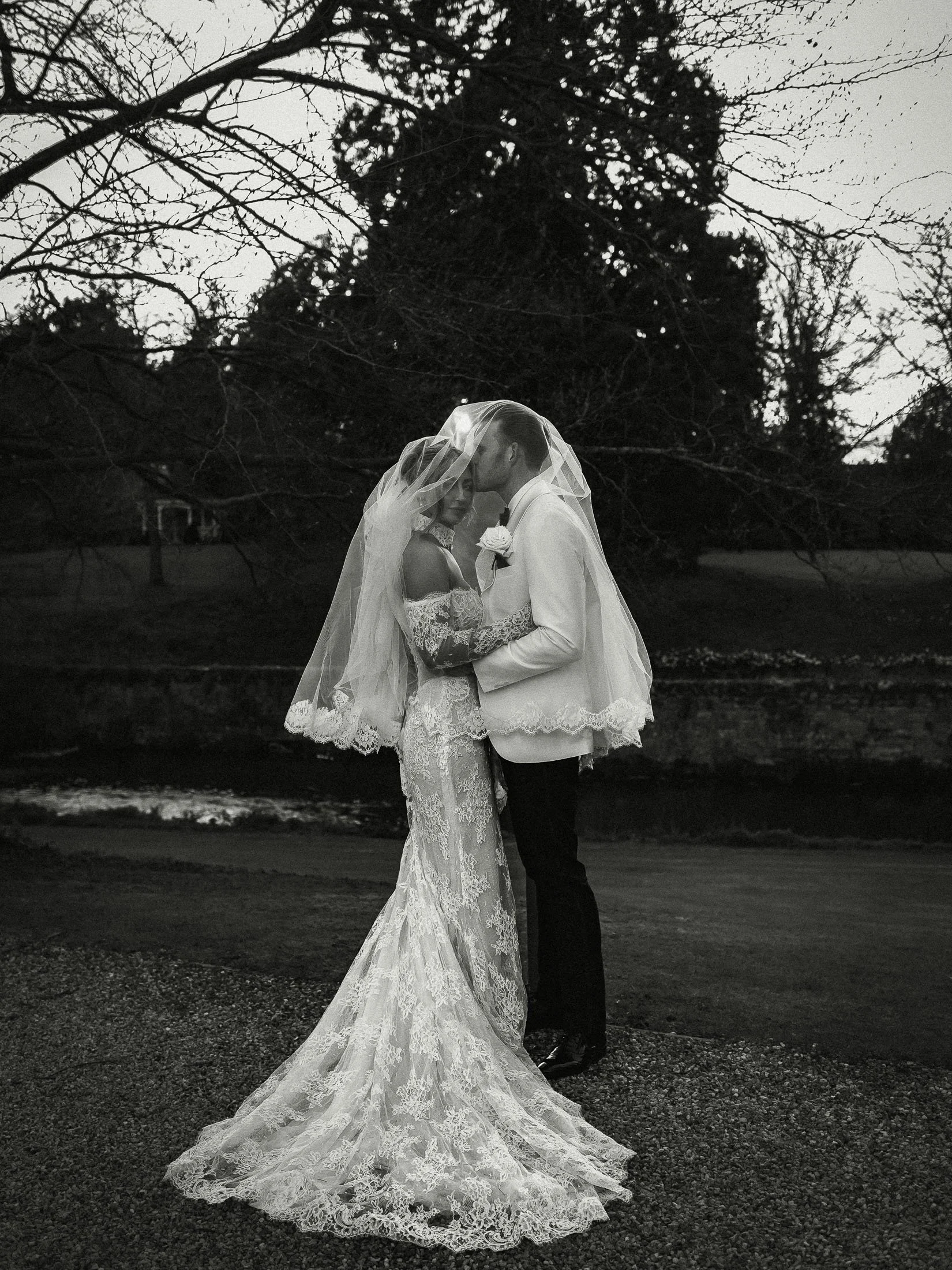 Wedding photography and videography for The Orangery Maidstone as a groom in white tuxedo kisses the forehead of his bride underneath a veil.