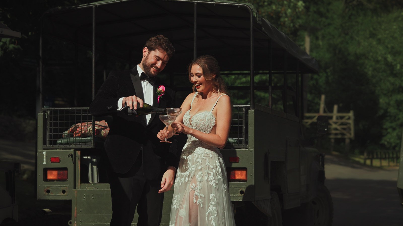 A groom wearing black tie pours Champagne into a glass held by his bride in a timeless editorial shot.