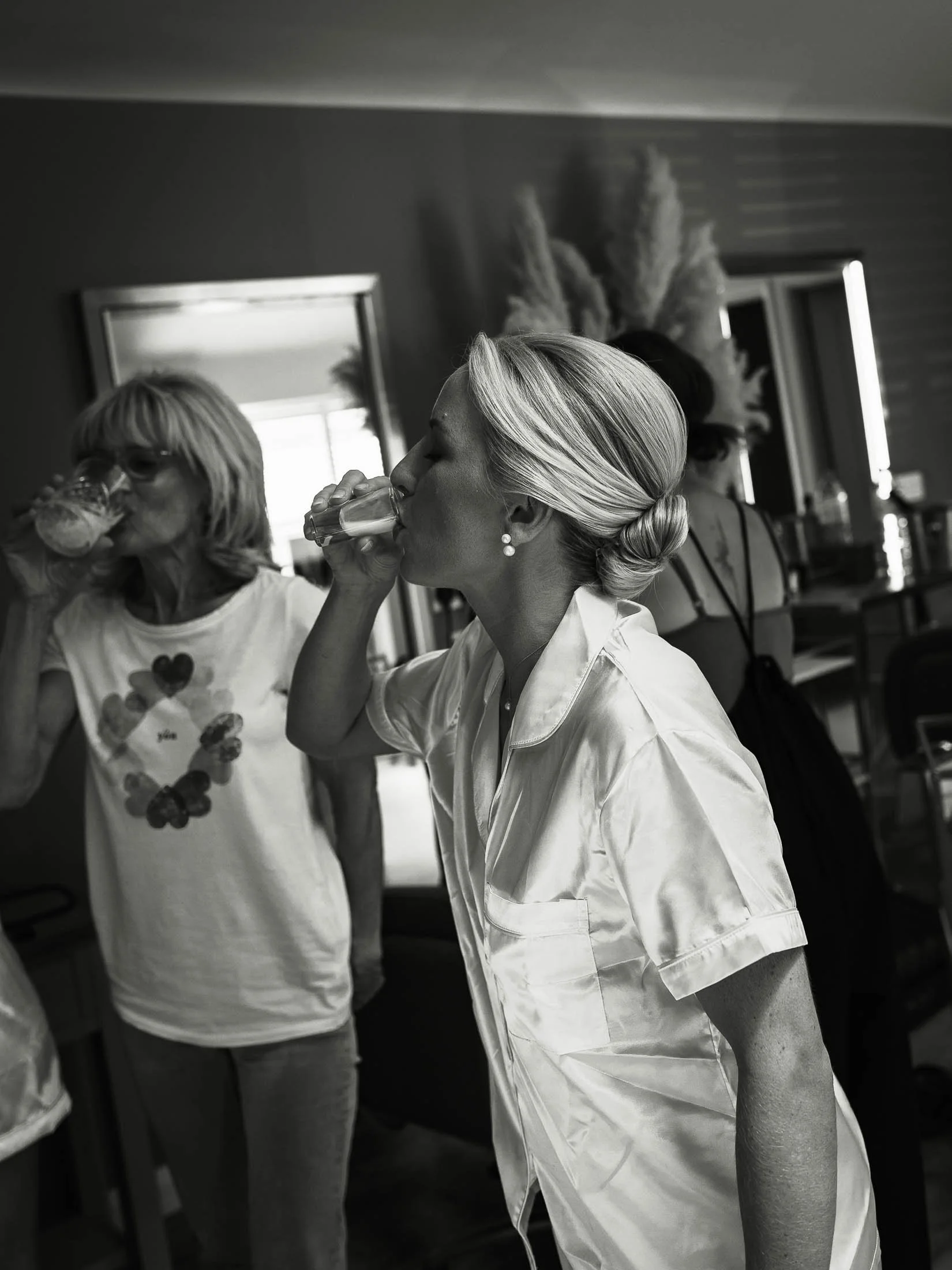 A natural wedding moment in a black and white aesthetic, showing a bride drinking a shot with her bridesmaids on her wedding morning at Winters Barns.