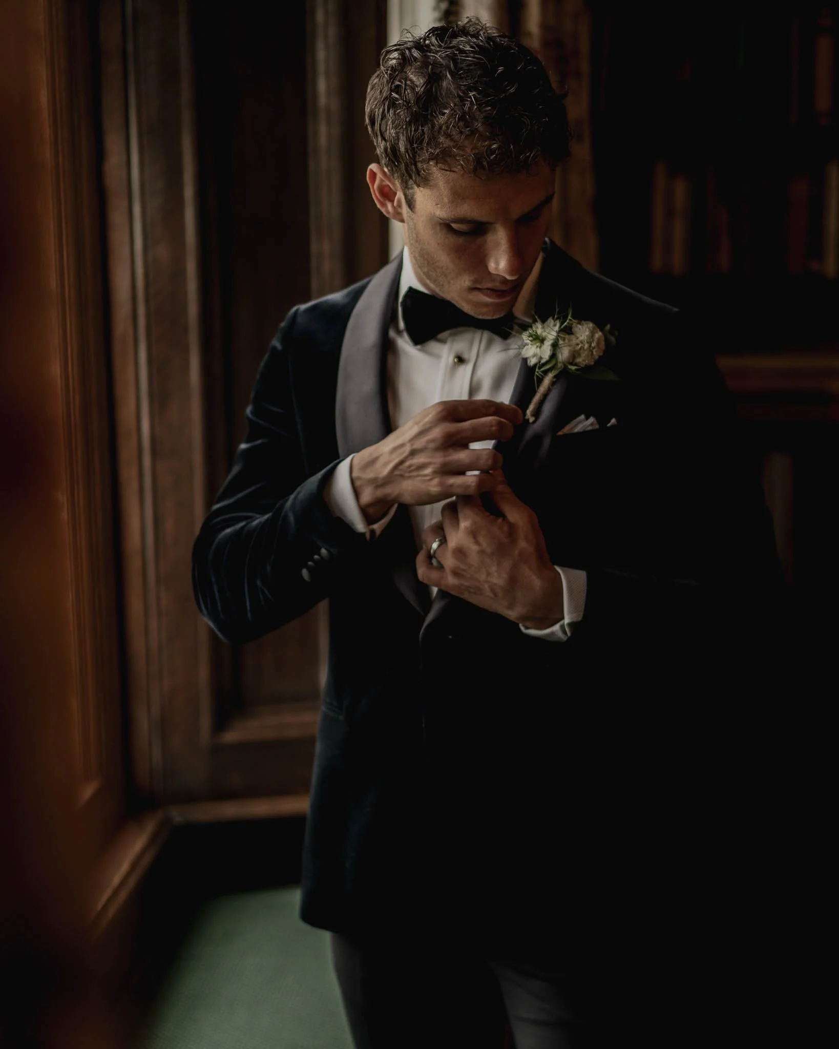 Fine art wedding photography of groom adjusting cufflinks in minimal natural light.