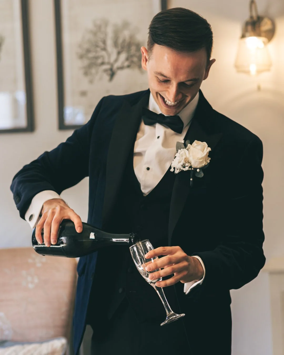 a wedding photography and videography team capture a groom in black tie pouring champagne.