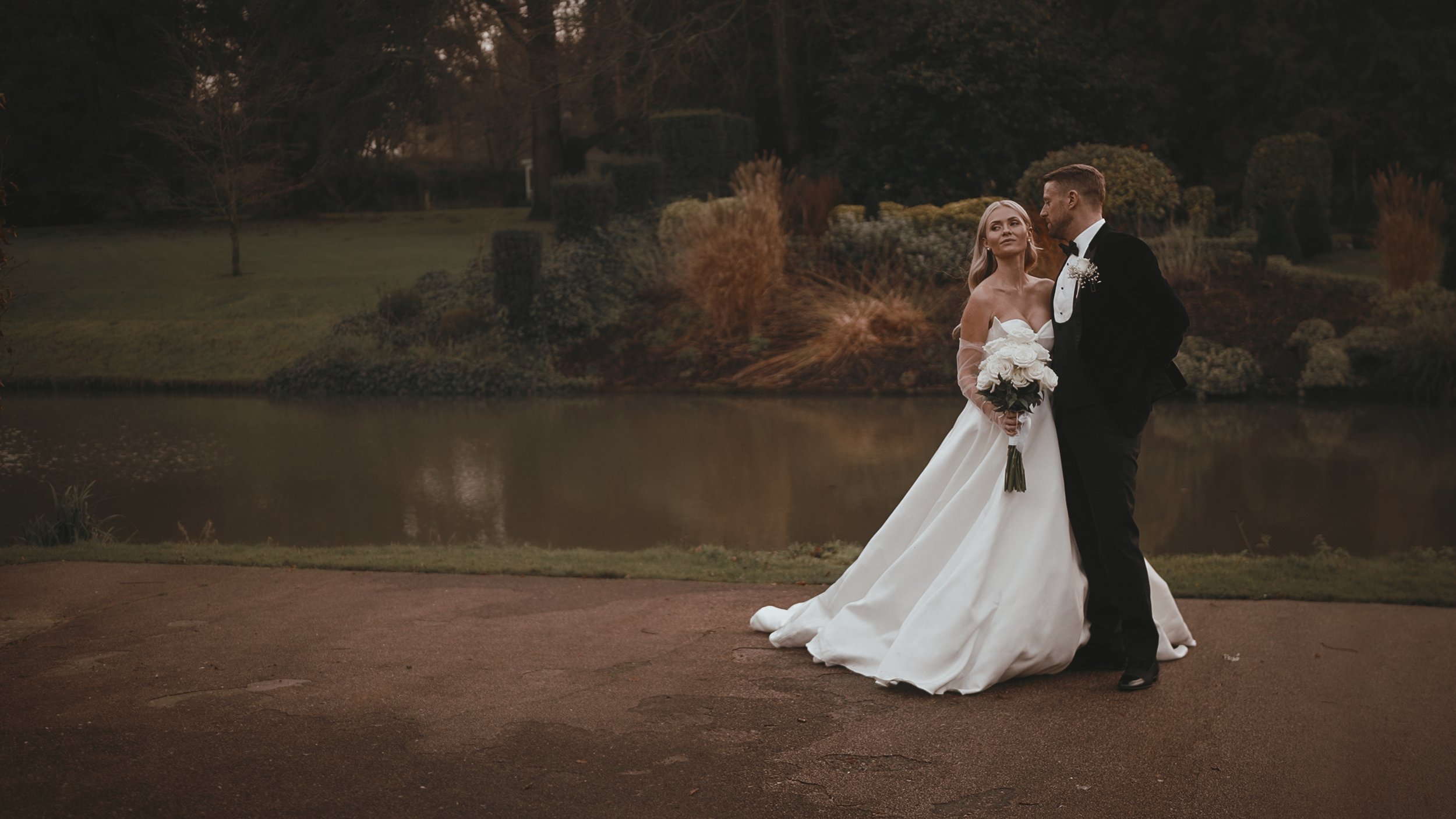 A couple pose elegantly together by the lake at The Orangery, Maidstone in Kent, for a wedding videography moment.