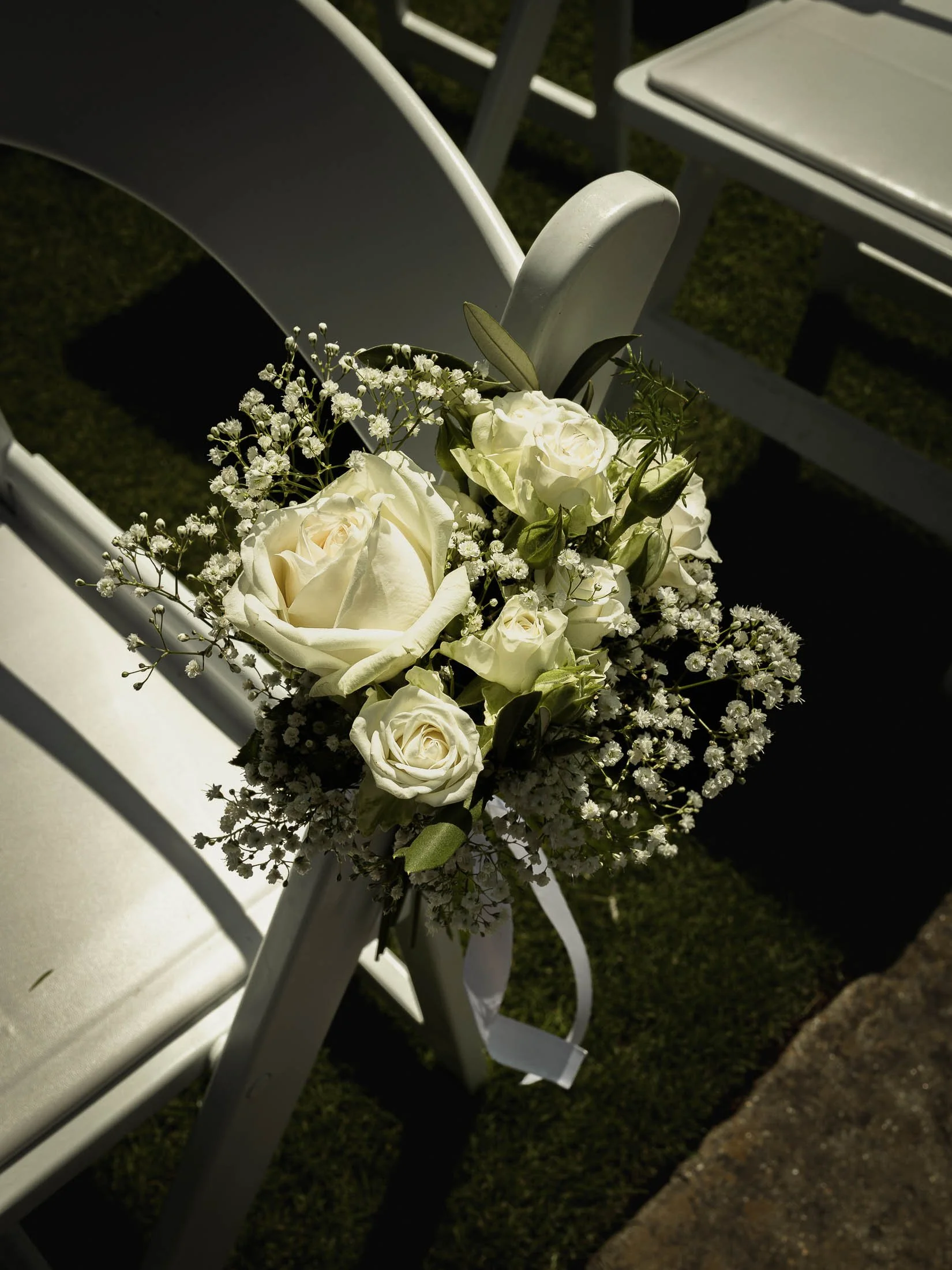 Summer outdoor wedding ceremony florals attached to white chairs during a Winters Barns wedding in Kent.