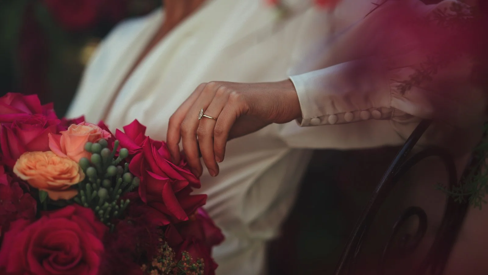 A close up fine art wedding shot of a brides wedding ring as she holds her bright pink and red bouquet.