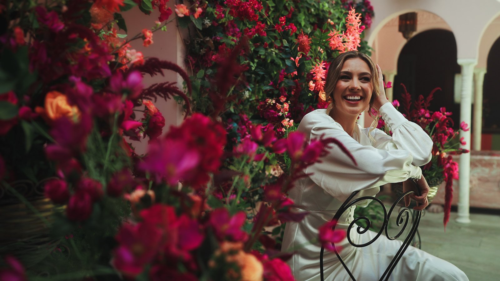 Fashion-focussed bridal portrait as she smiles surrounded by bold, bright pink florals.