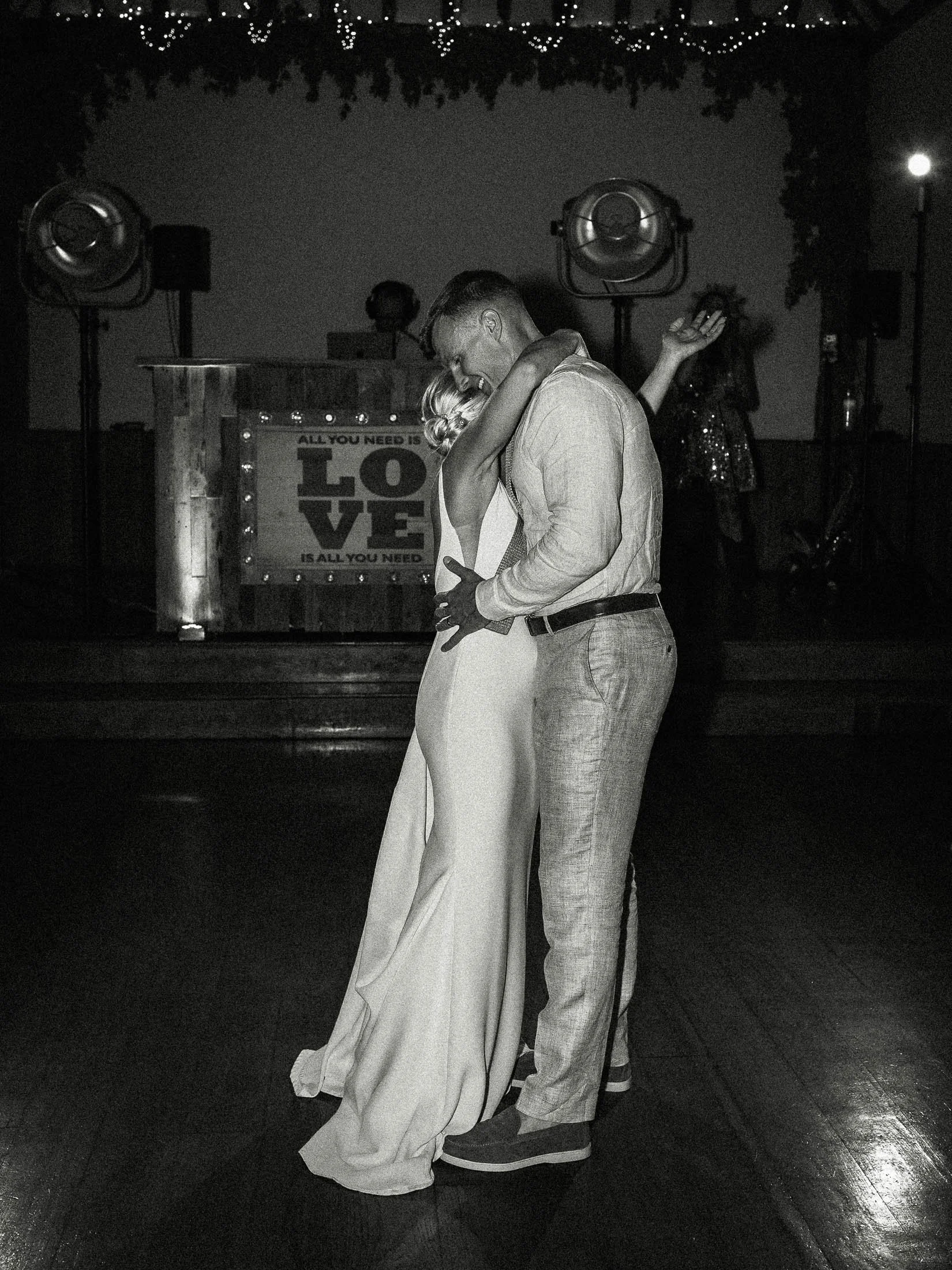 An editorial black and white wedding photograph of a bride and groom embracing during their first dance at Winters Barns wedding venue in Canterbury, Kent.