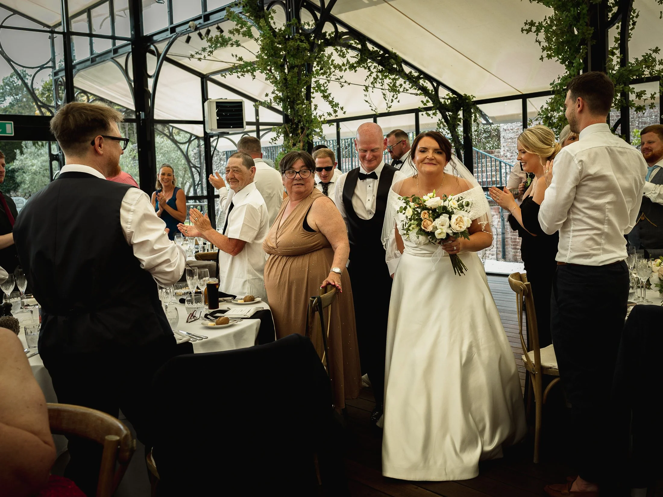 A bride and groom enter their wedding breakfast at the Glass Orangery at Port Lympne Hotel.