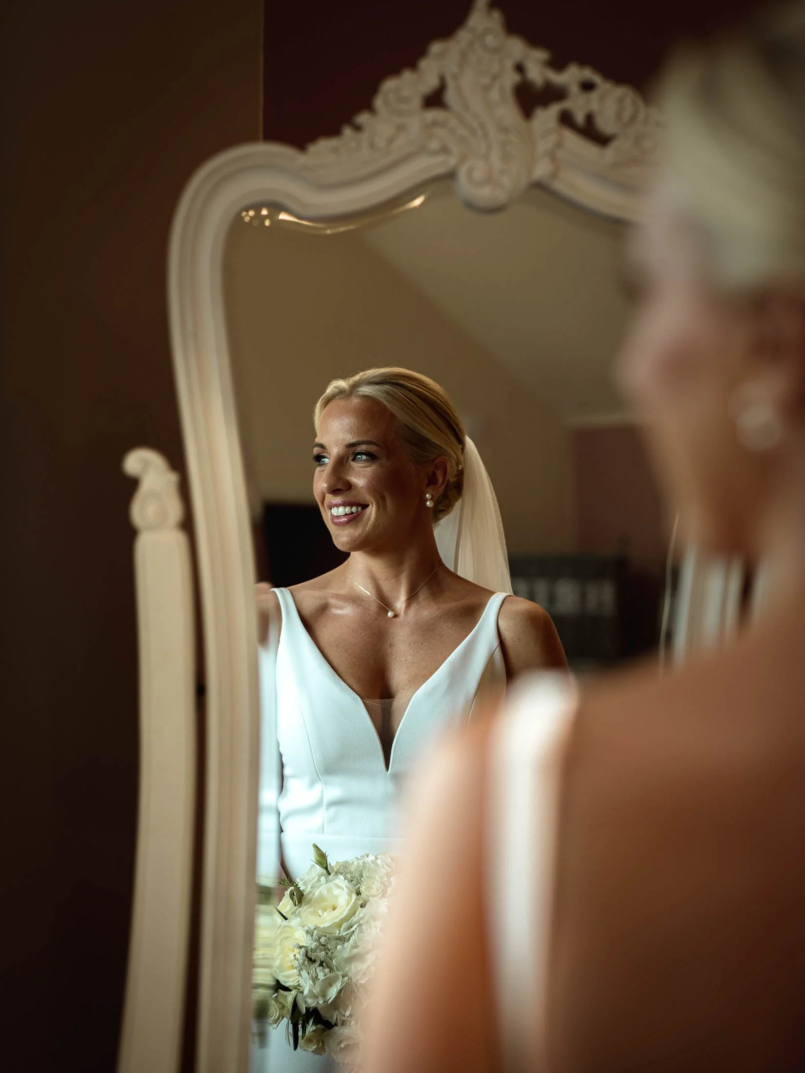 A bride smiles in her wedding dress as she is reflected in a mirror at Winters Barns in Kent.
