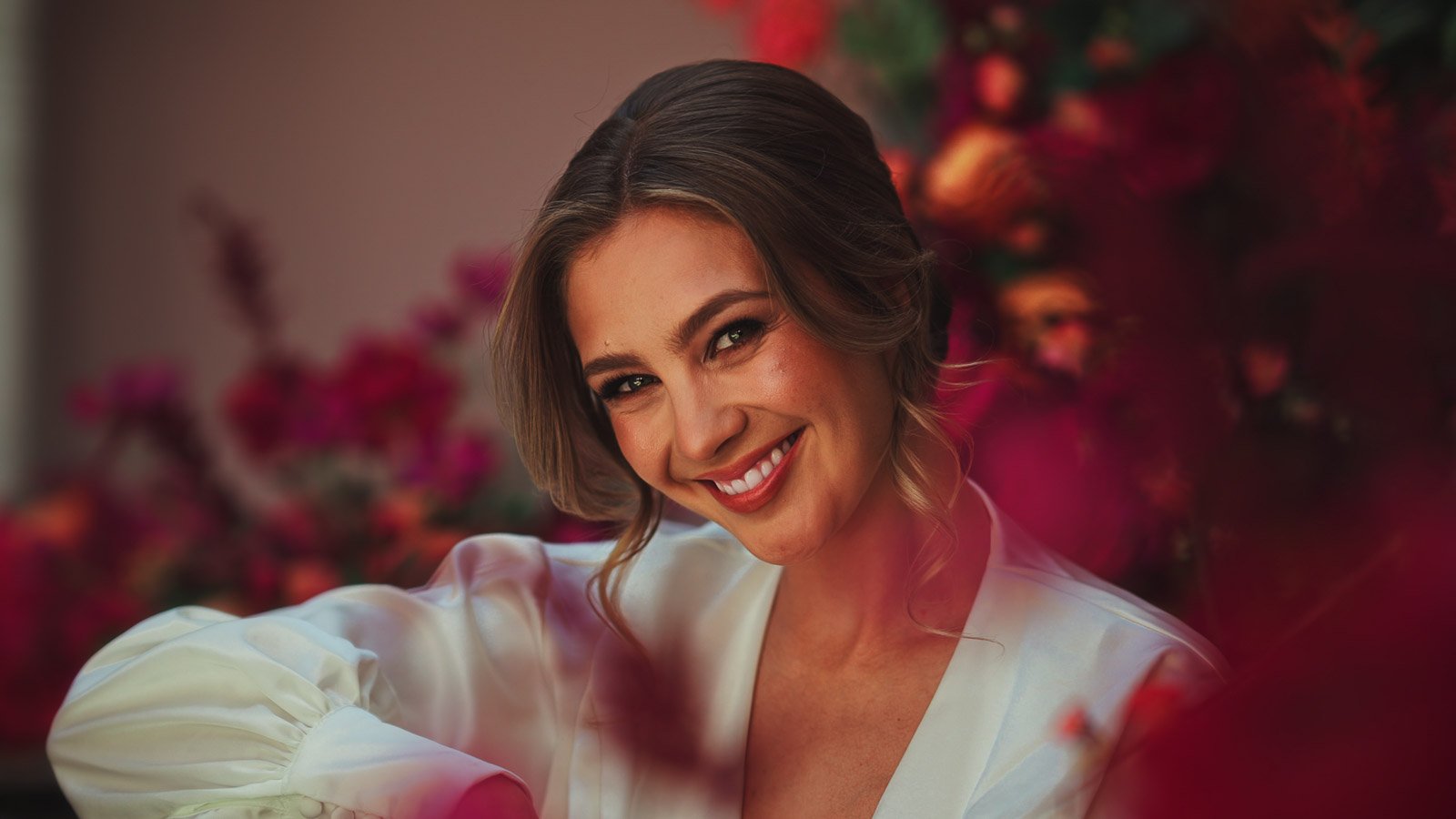 Bride in minimal dress with vivid pink and red colour palette surrounding her smiles directly at the camera.