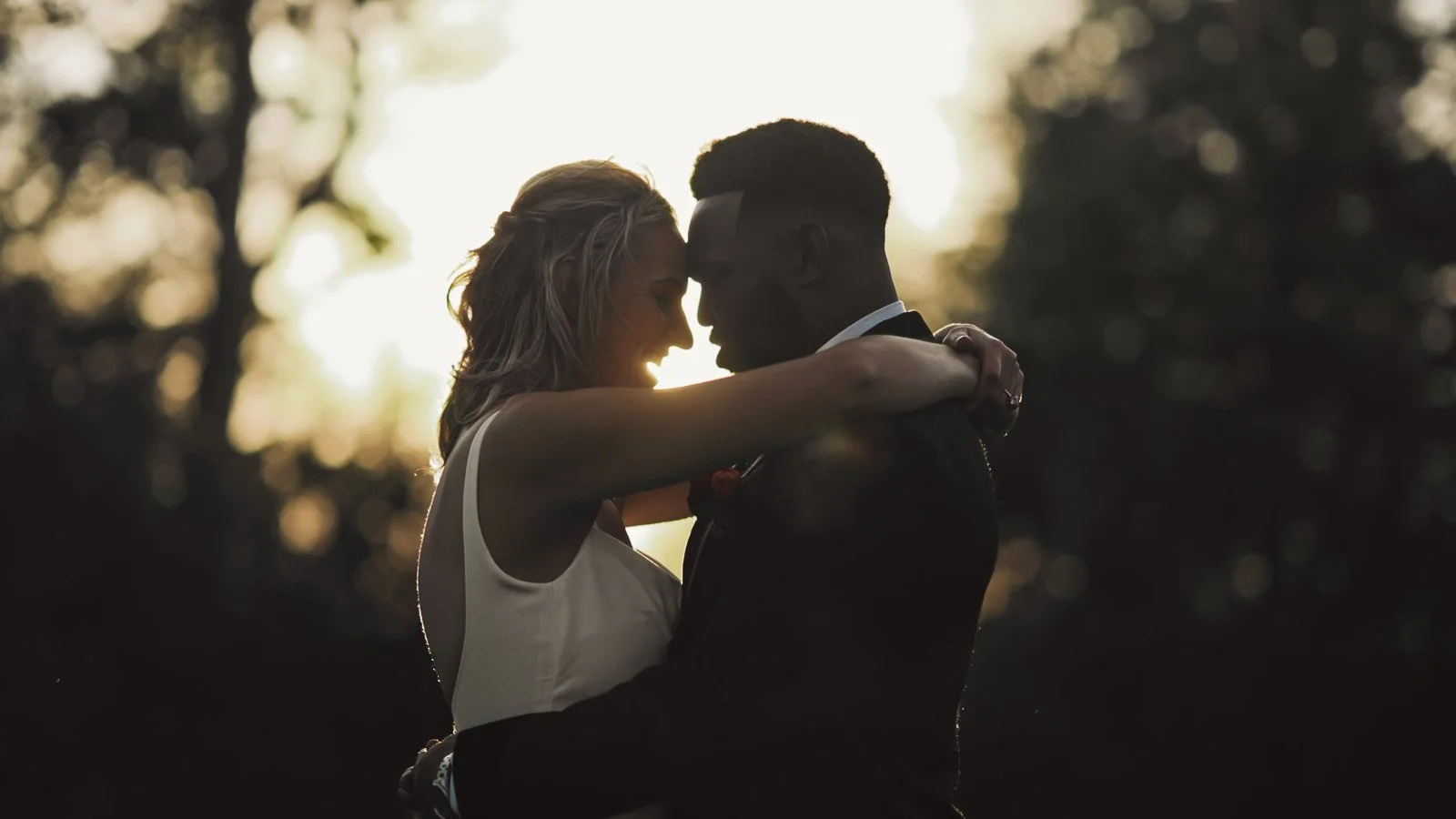 An editorial portrait of a bride and groom by the River Thames during their colourful riverside wedding day. The couple are silhouetted by the setting sun.