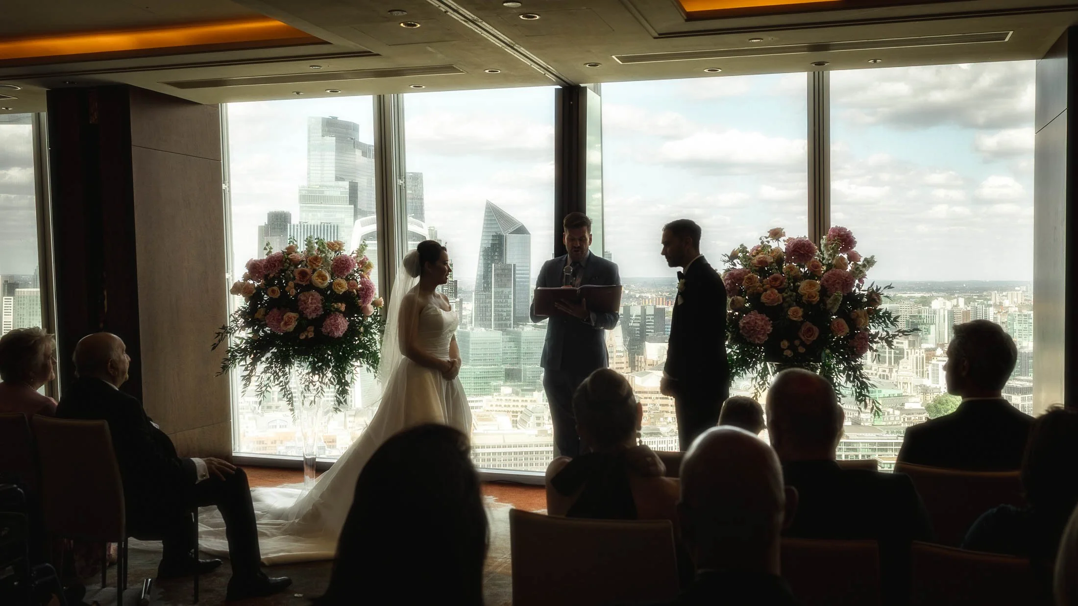 A quiet moment during an indoor wedding ceremony at the Shangri-La The Shard as the bride and groom read personal wedding vows and the background shows the City of London skyline.