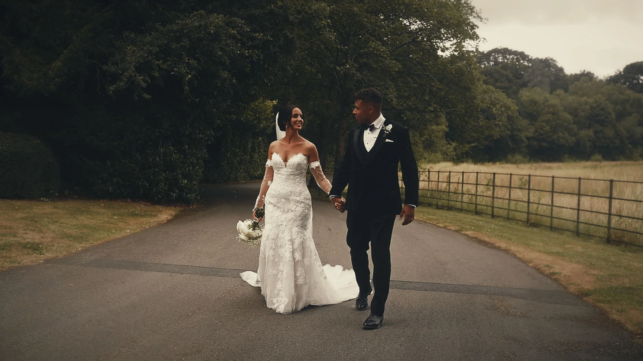 A bride and groom smile and walk together during their black tie wedding day at Botleys Mansion in Surrey. A screenshot image taken from their cinematic wedding film.