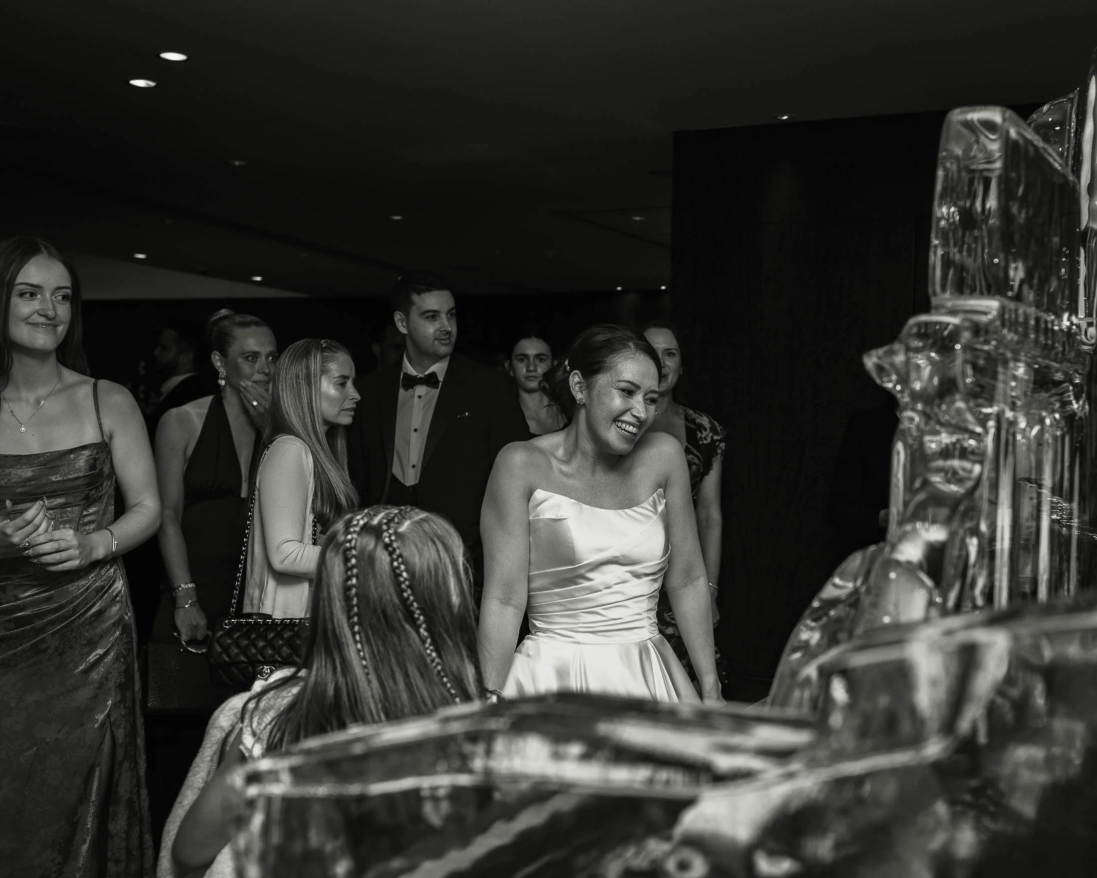 A black and white editorial wedding photograph showing a bride smiling surrounded by her guests during her London wedding.