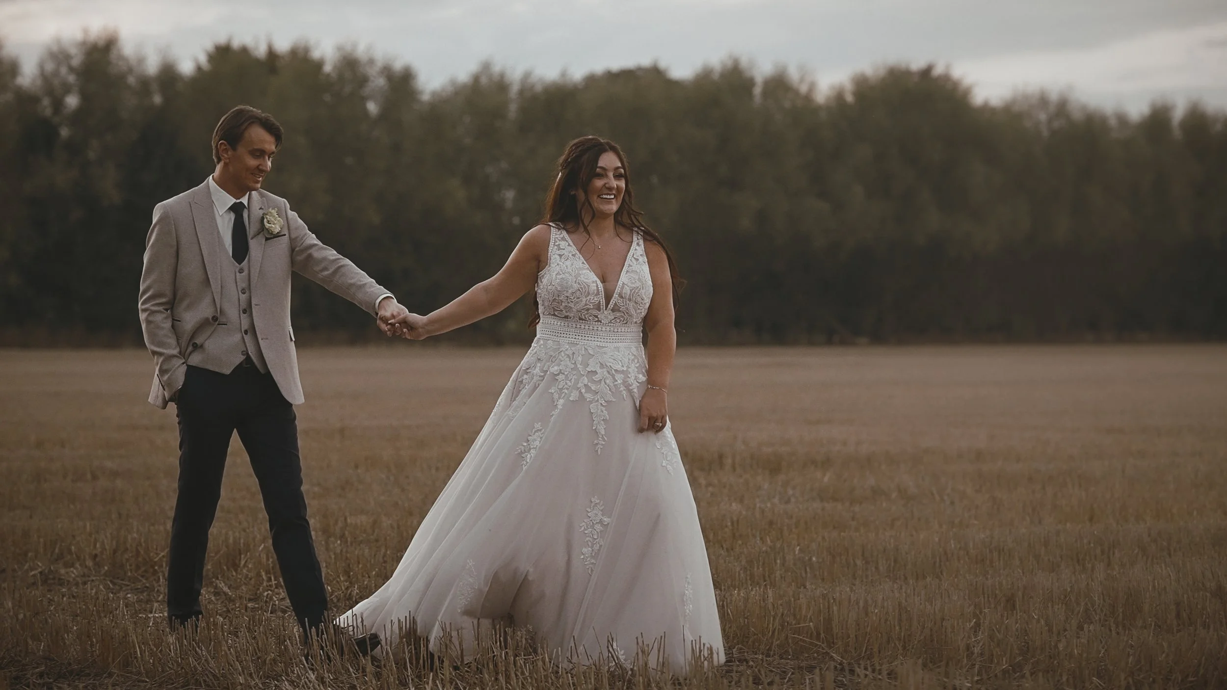 A bride leads the groom through an open field at sunset during a Winters Barns wedding.