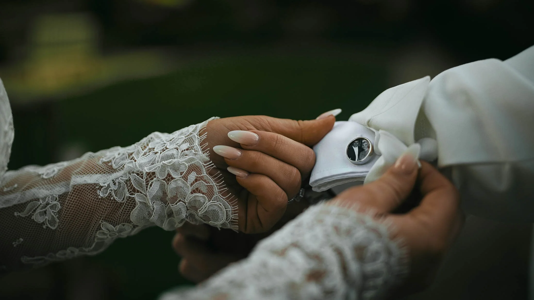 The bride holding the cuffs of the grooms jacket, showing his personalised cufflinks which have a picture of his late grandparents within them.