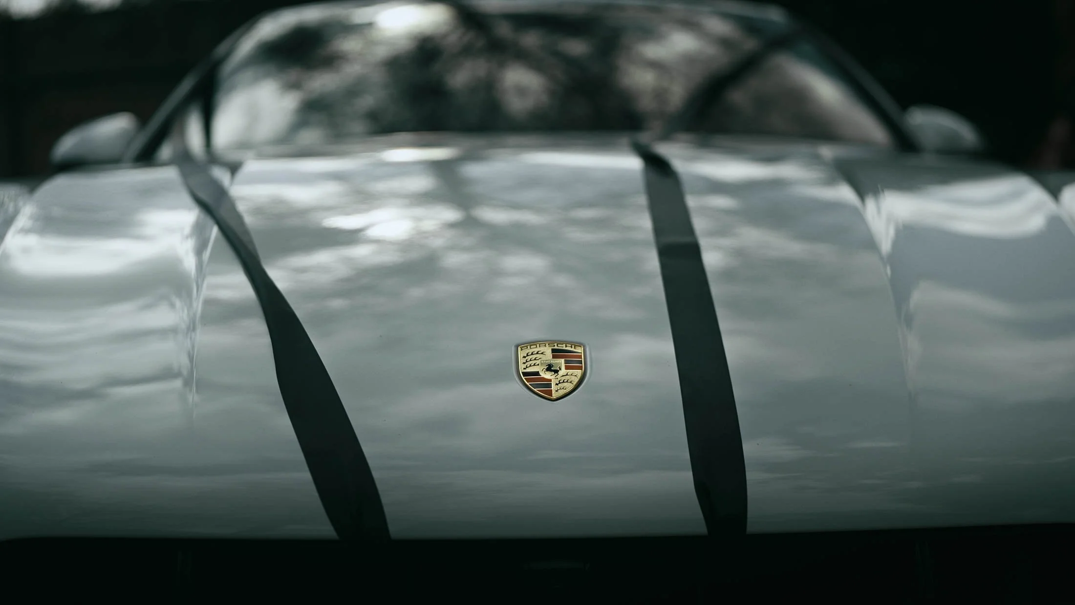 A white Porsche wedding car with black ribbons flowing in the wind with tree reflections in the bodywork.