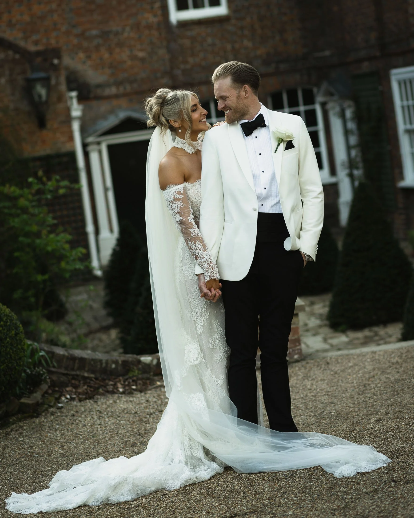 Editorial portrait of a groom in white tuxedo with his bride in the formal gardens of The orangery Maidstone captured by a photo and film team.