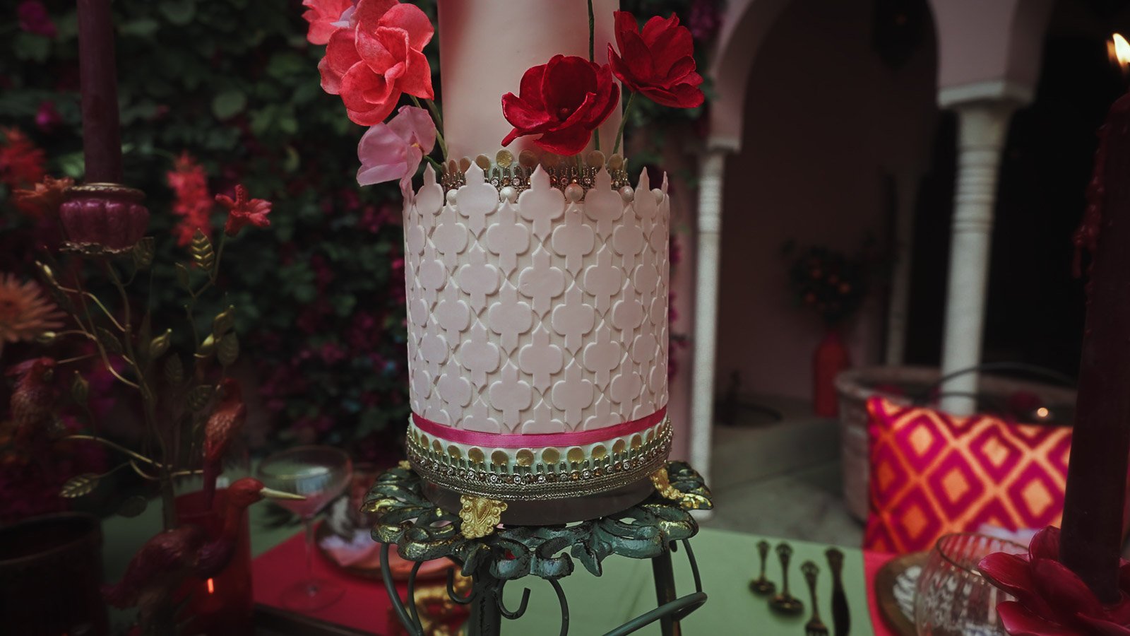 A luxurious wedding cake sits amongst bright pink and red florals and decor, during a colourful outdoor summer wedding in Kent.
