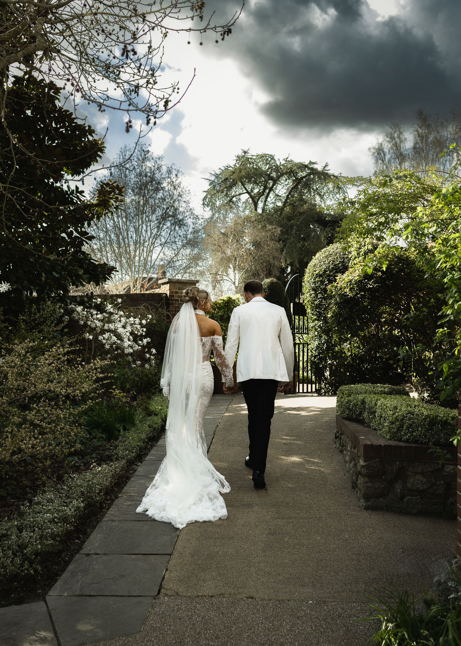 A bride and groom walking through the formal gardens of The Orangery Maidstone during their black-tie wedding.