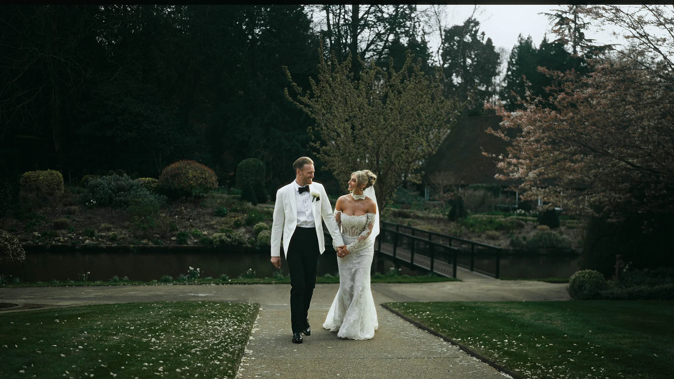 A bride and groom walking though the grounds of a luxury UK wedding venue, in a natural moment from their wedding film which focusses on story and narrative.