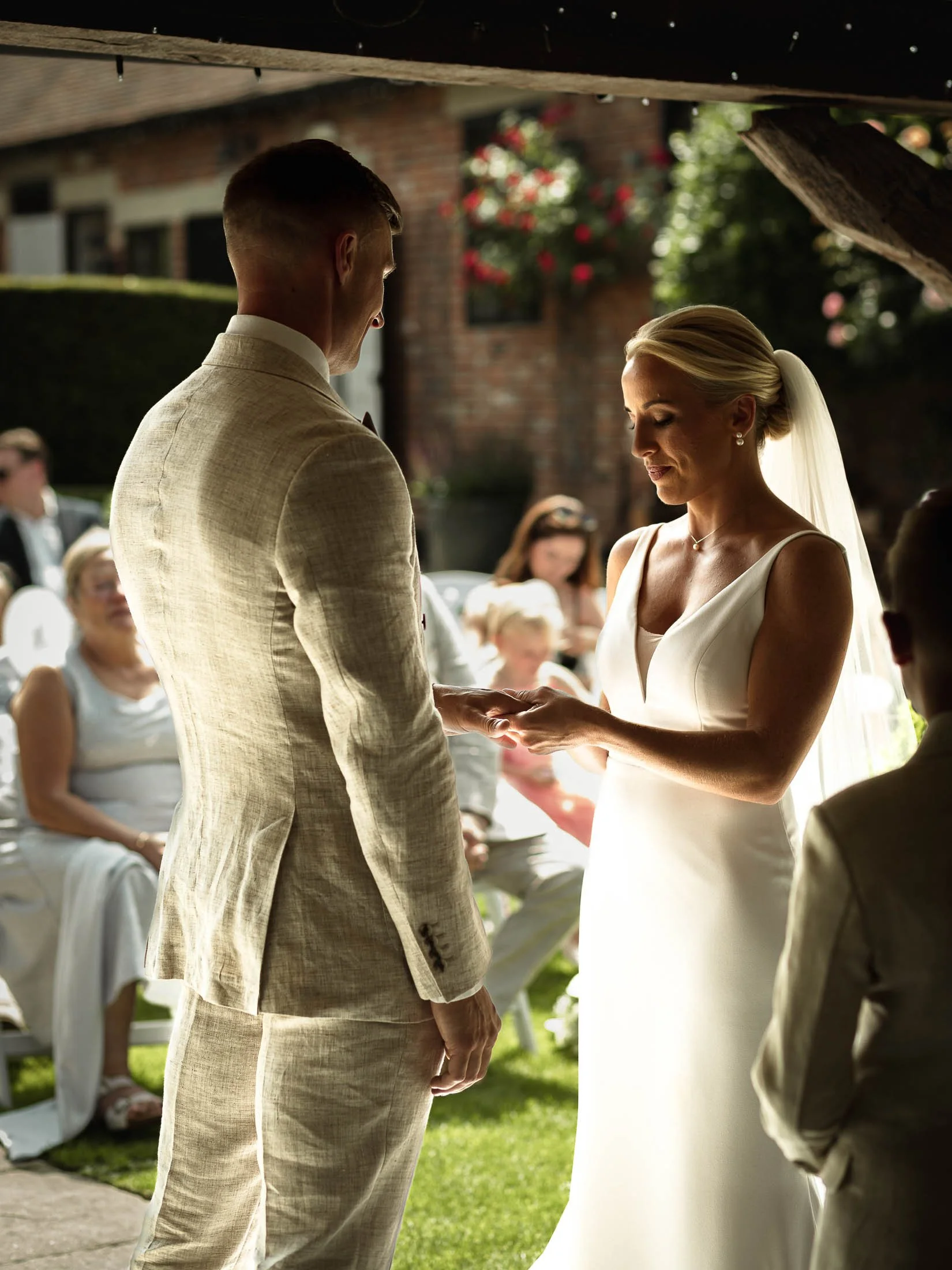 A bride and groom exchanging rings and vows during their outdoor summer wedding ceremony at Winters Barns in Kent, captured by both photography and videography as a part of a cohesive media team.