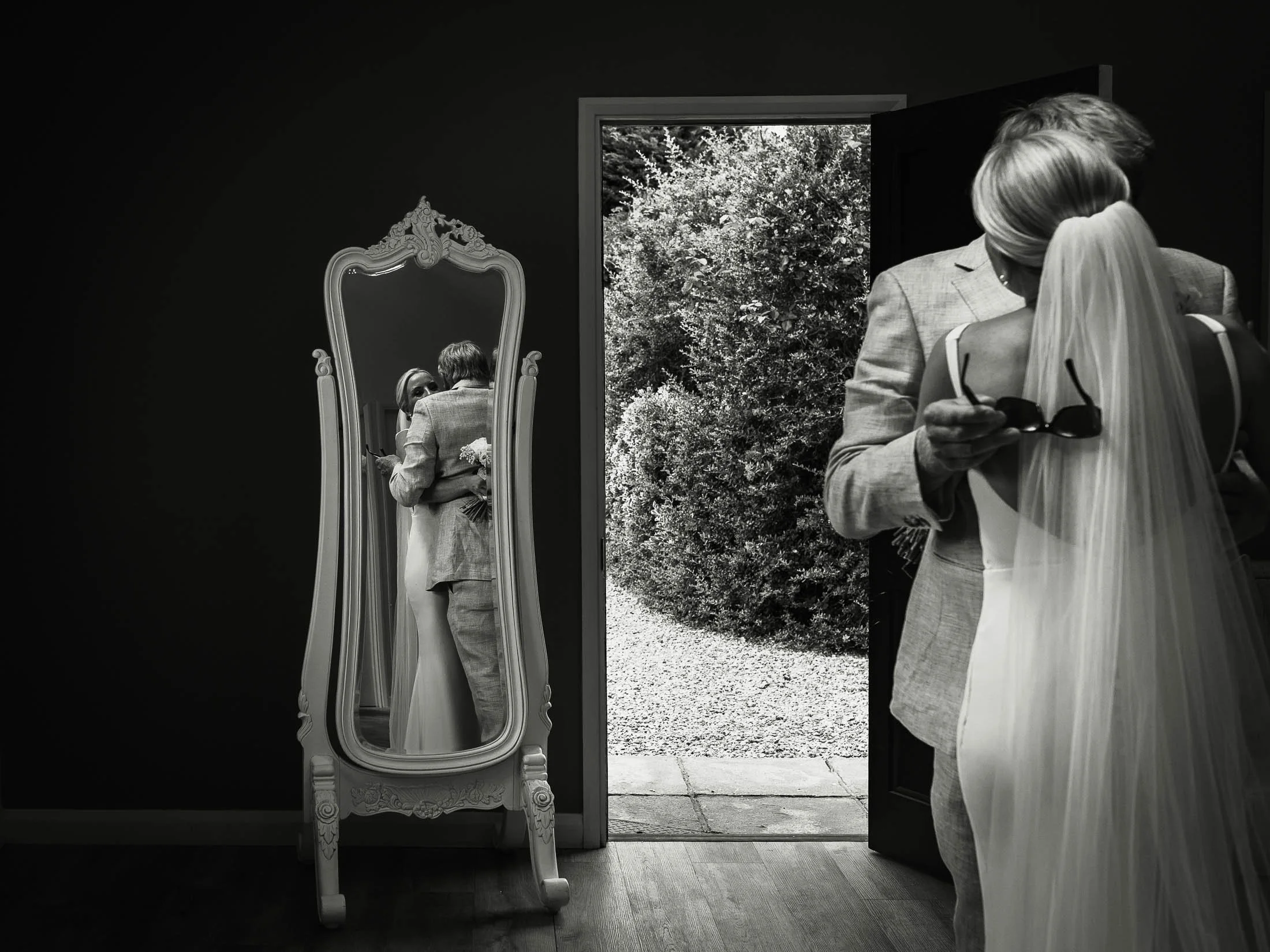 An artistic and highly emotive wedding photograph from Winters Barns, showing the moment a father see's the bride in her wedding dress for the first time. As they embrace, you can see their reflection in the mirror.