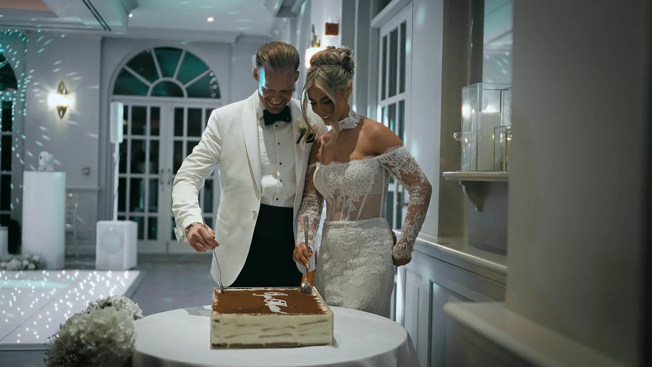 A bride and groom cut into their tiramisu wedding cake during evening celebrations at The Orangery, Maidstone, captured and told as part of their storytelling wedding film.