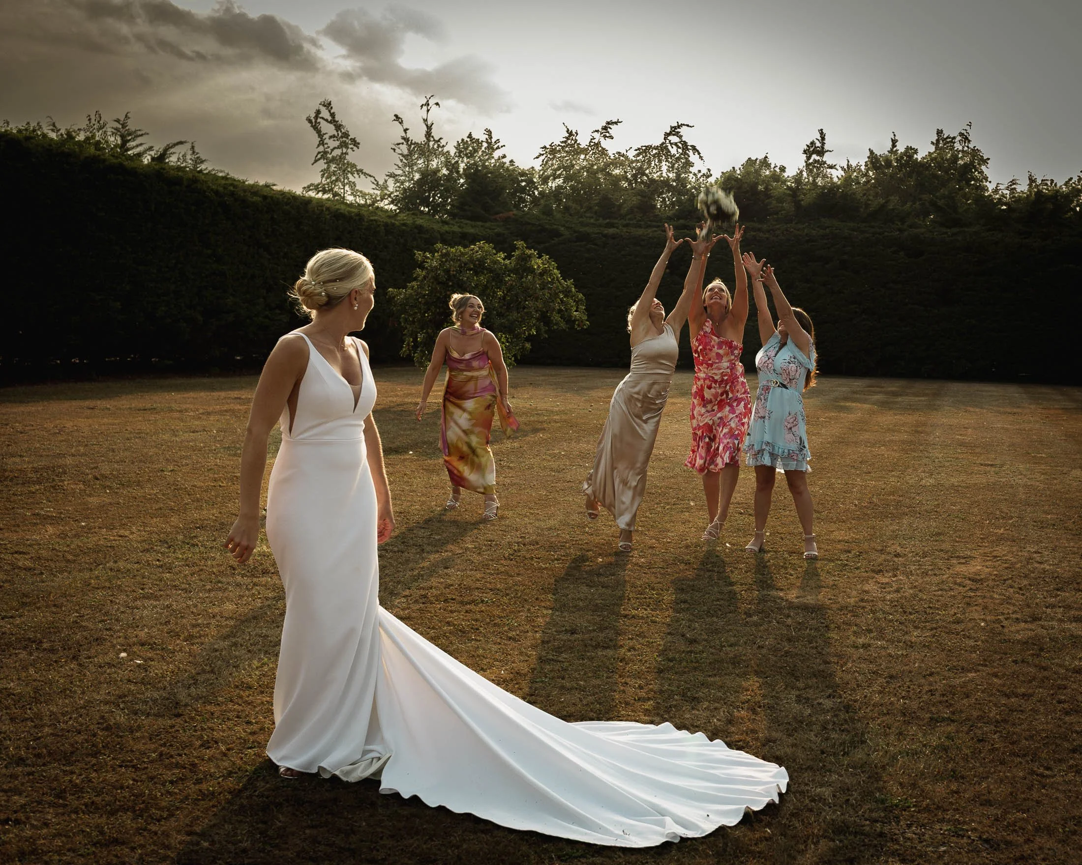 A candid and funny moment as a bride throws her bouquet and her female wedding guests attempt to catch it in the grounds of Winters Barns.