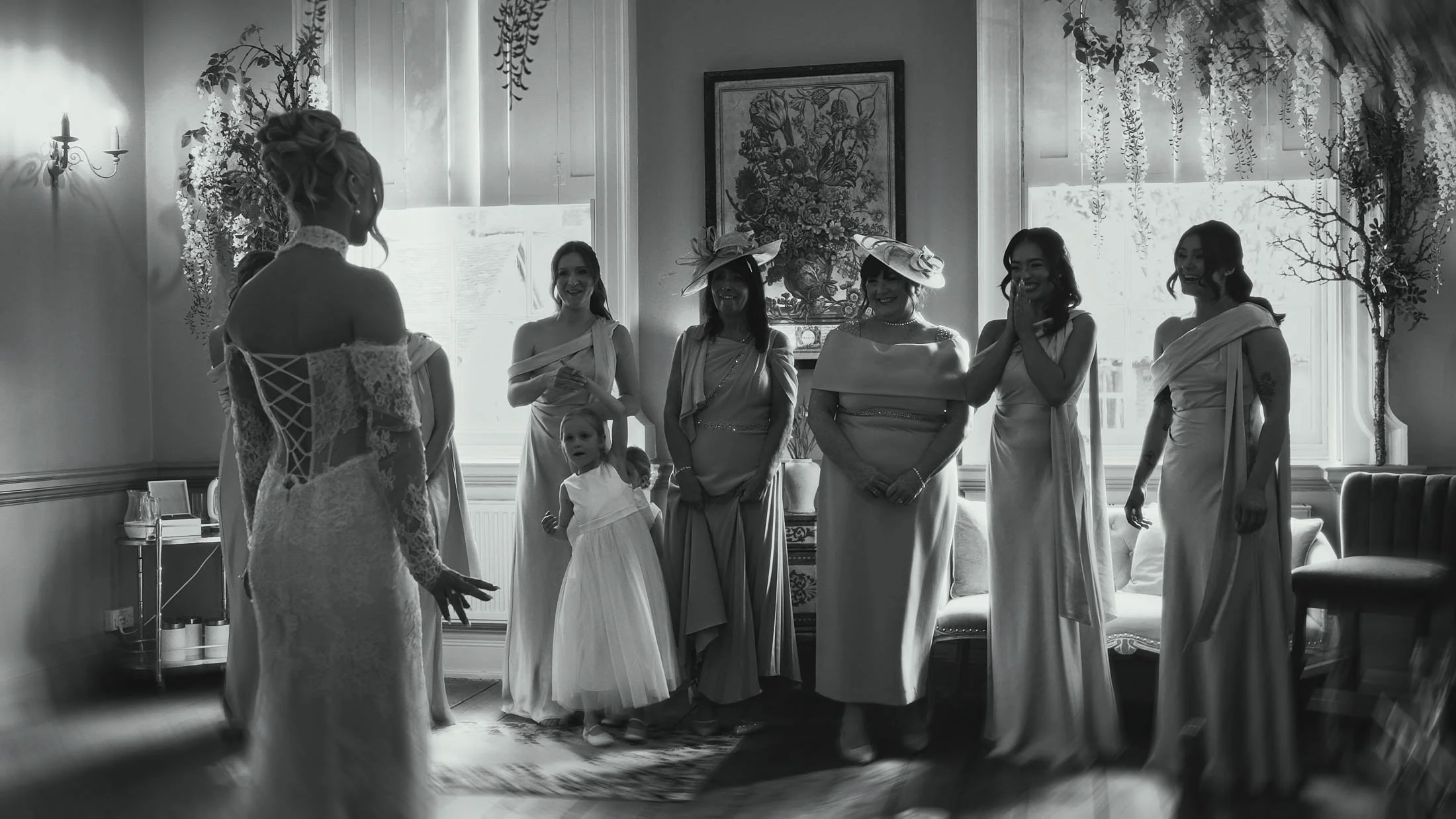 A black and white highly emotional moment taken from a storytelling wedding film as a bride reveals her dress to her Mother and bridesmaids.