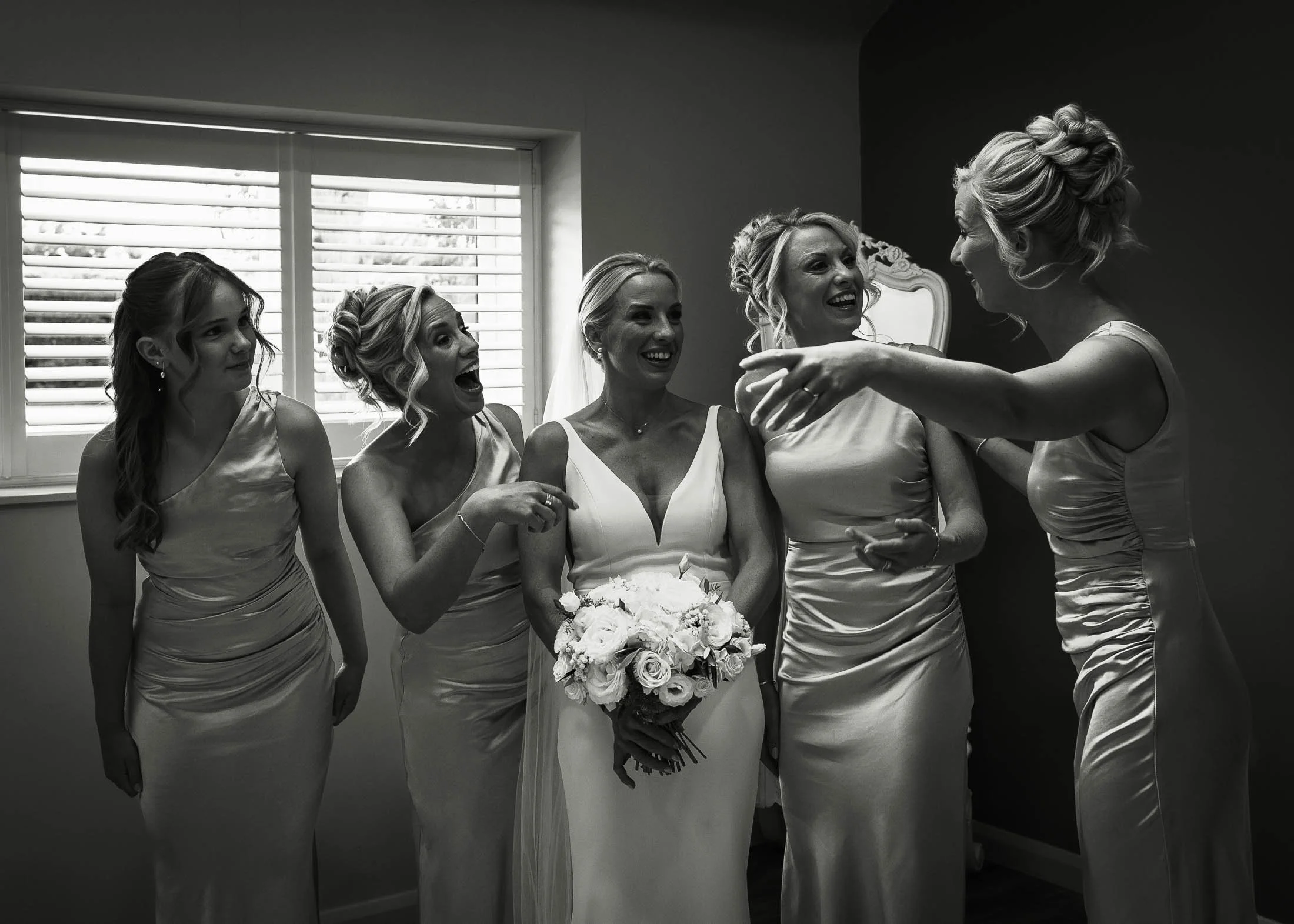 A black and white editorial wedding photograph of bridesmaids and the bride laughing just before the wedding ceremony at Winters Barns.