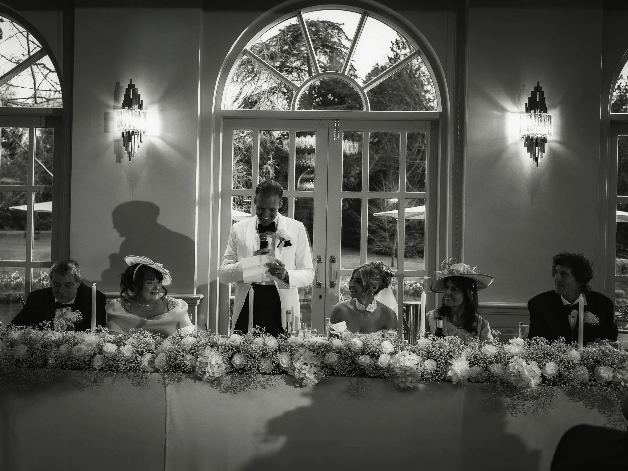 A groom in white tuxedo delivers a speech during a wedding reception at The Orangery Maidstone.