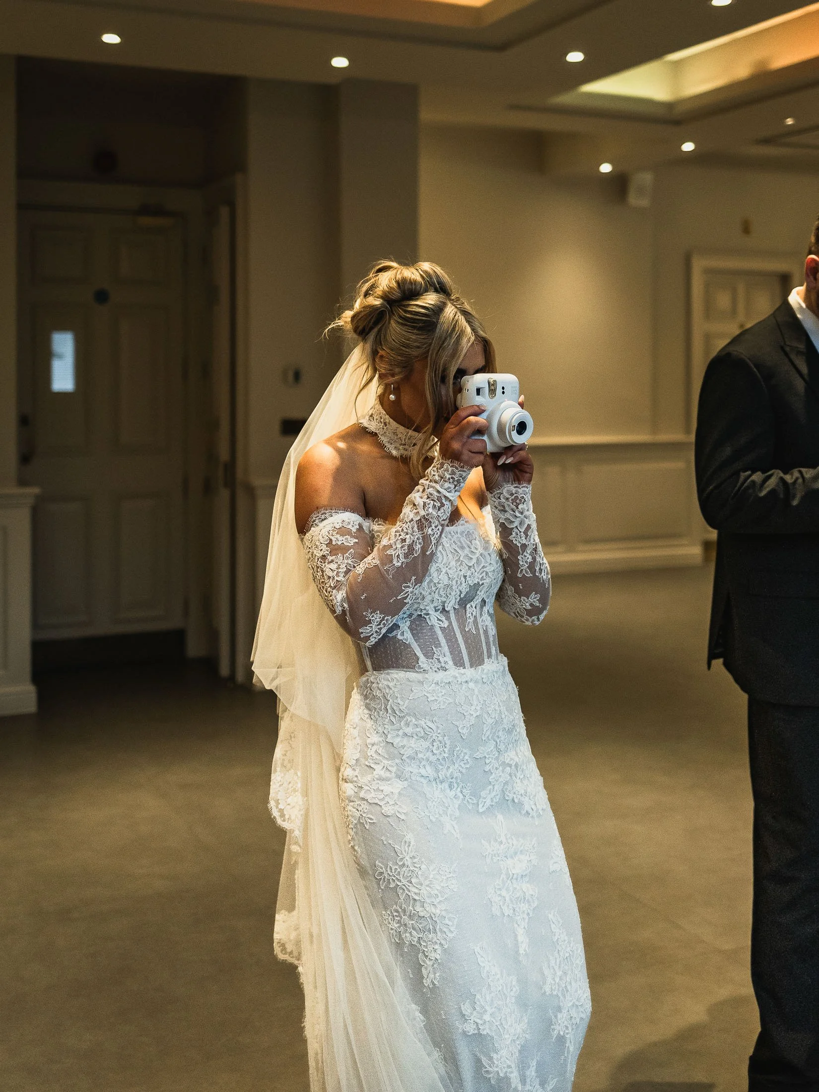 A candid moment of a bride taking a photograph with a camera during an indoor wedding reception at The orangery maidstone.