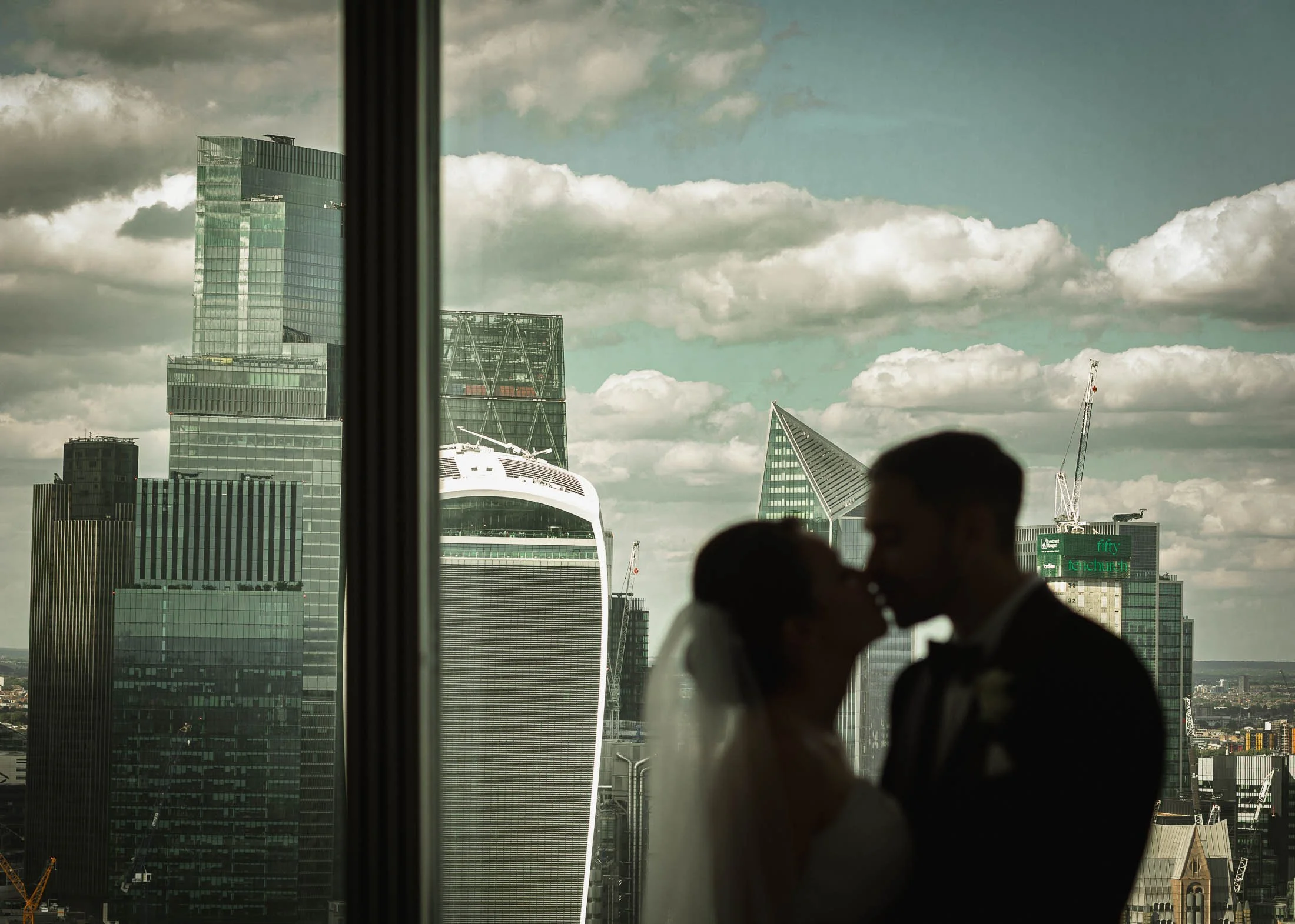 A couple are silhouetted as they kiss with the city of London skyline behind them. Captured from the 34th floor of the Shangri-La hotel at The Shard.