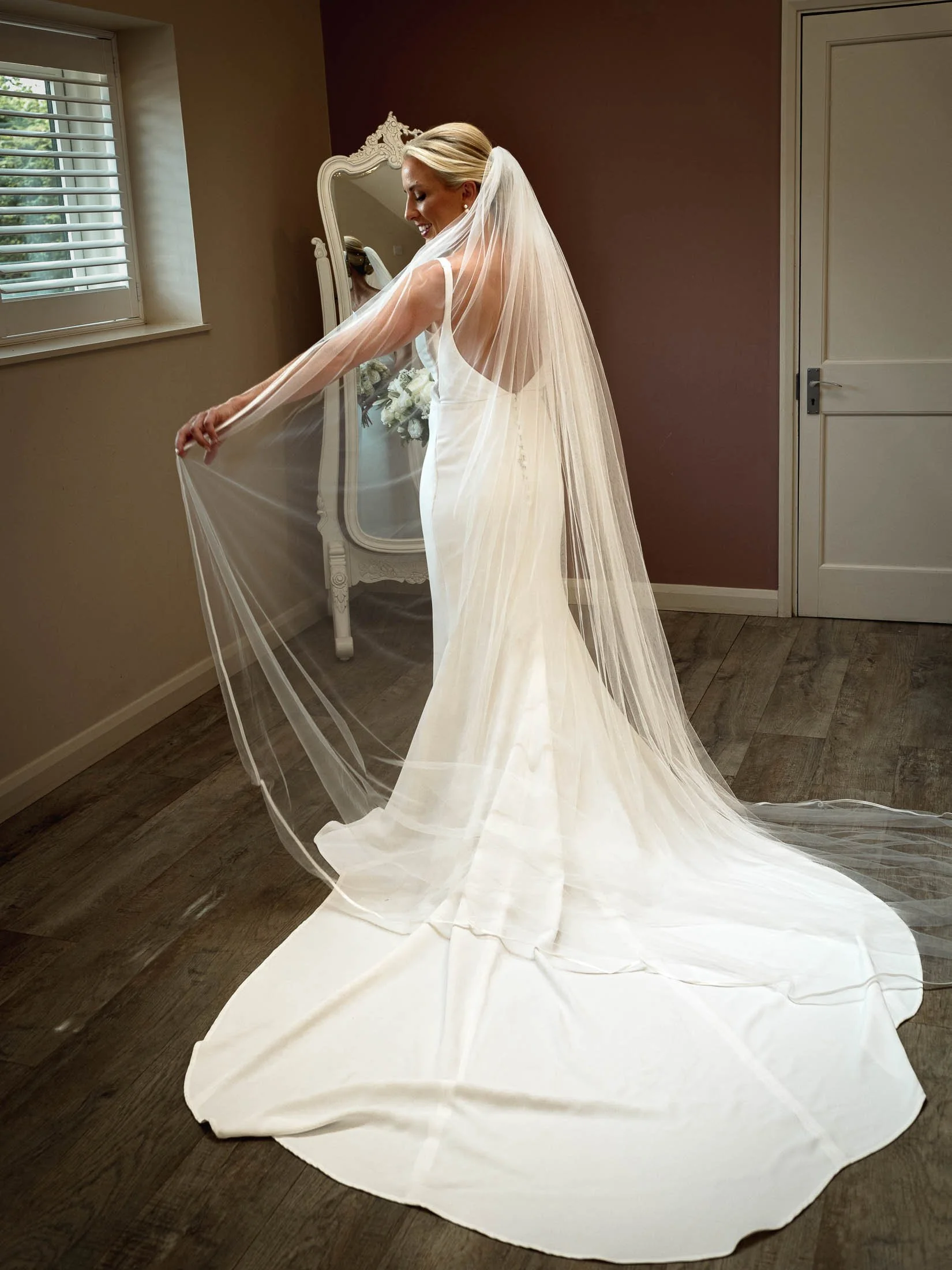 A full length portrait of a bride in her wedding dress and playing with her veil on her wedding morning at Winters Barns in Kent.