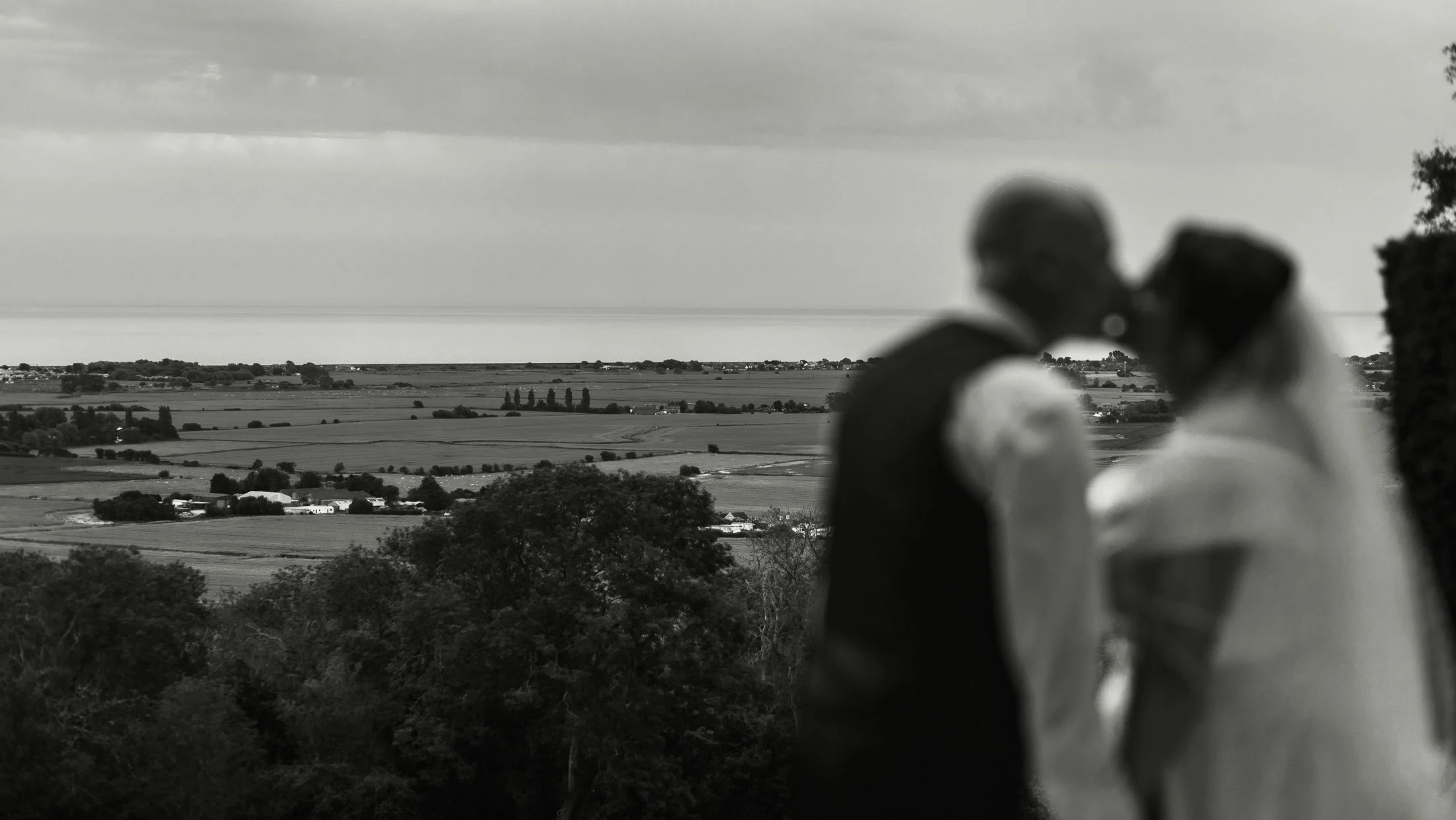 Lucy and Luke kiss as they are silhouetted against the view out towards the sea from Port Lympne Hotel.