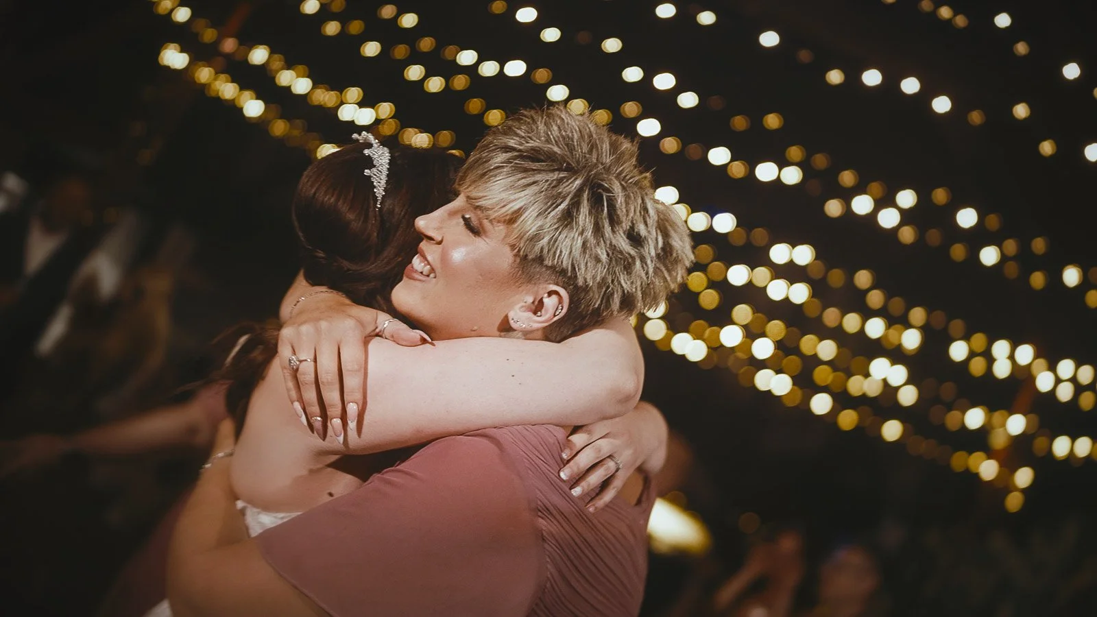 A bride embraces her bridesmaid during evening celebration energy inside Cooling Castle Barn wedding reception