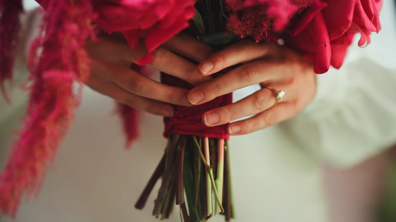 Close up detail shot of a brides hands holding a bold bright pink and red bouquet.