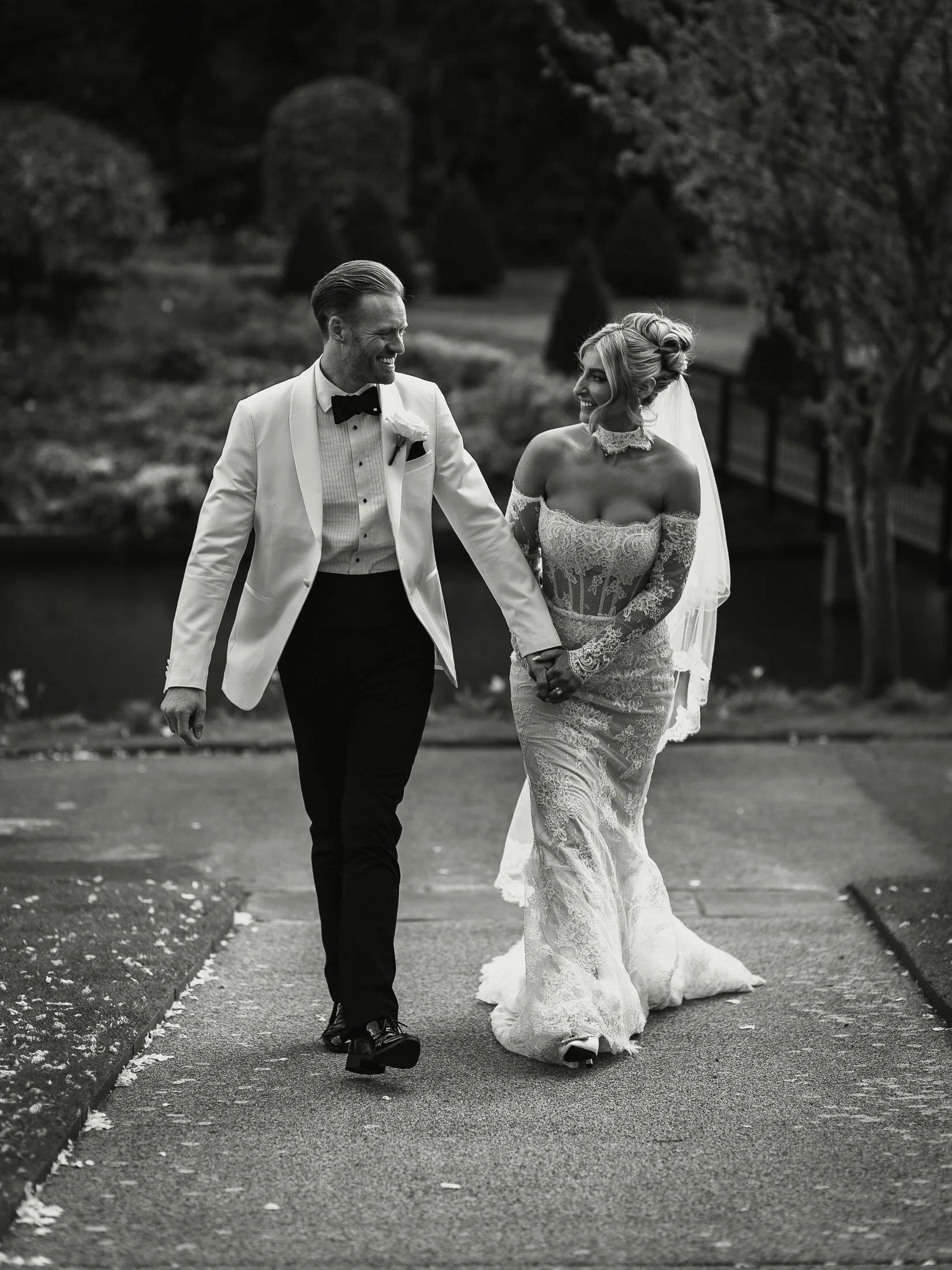Bride and groom walking together during their outdoor couples portrait session at the orangery Maidstone in a black and white editorial wedding image.