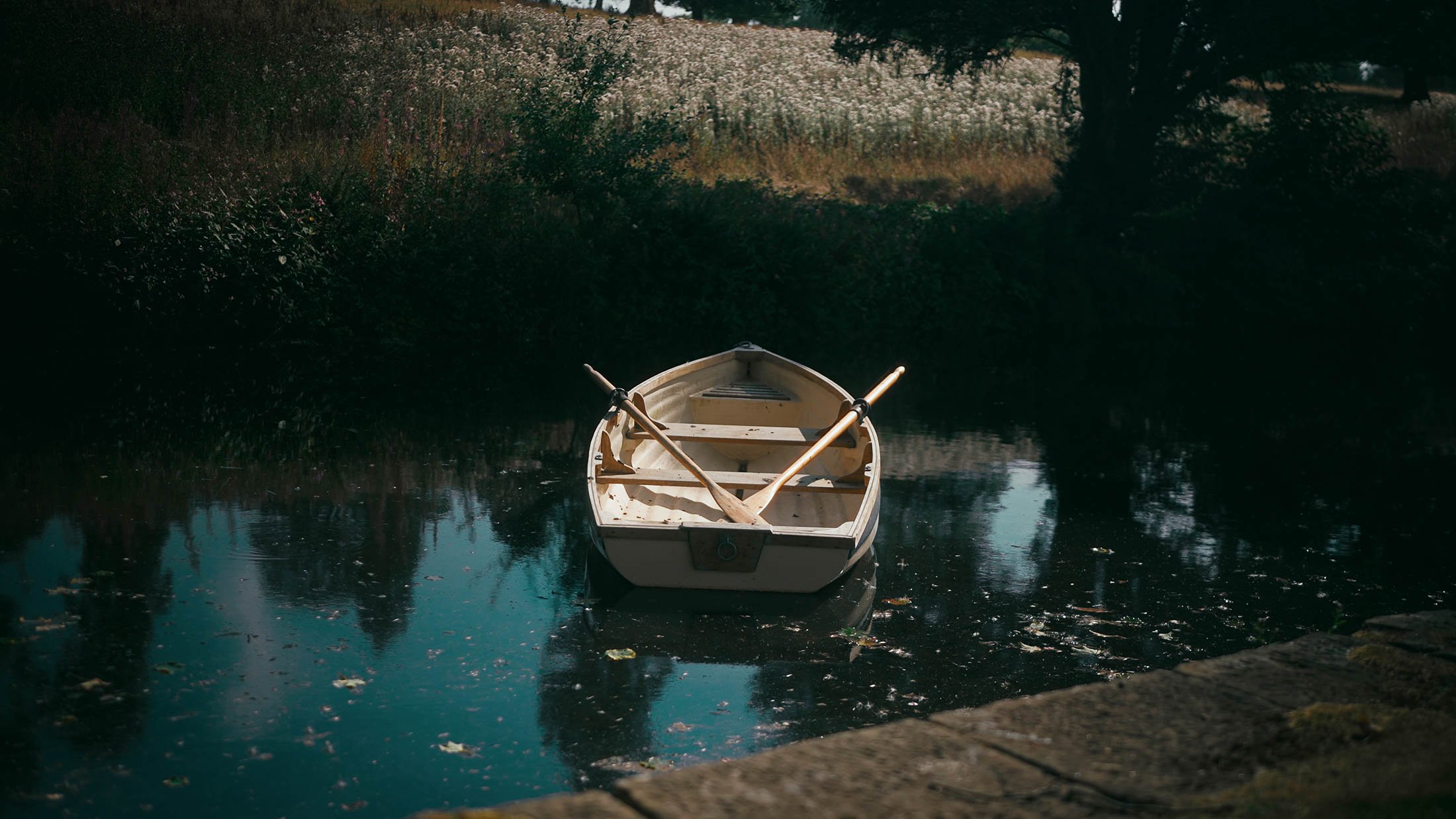 A small white boat floats in the river running alongside the driveway to Grantley Hall wedding venue in Yorkshire.