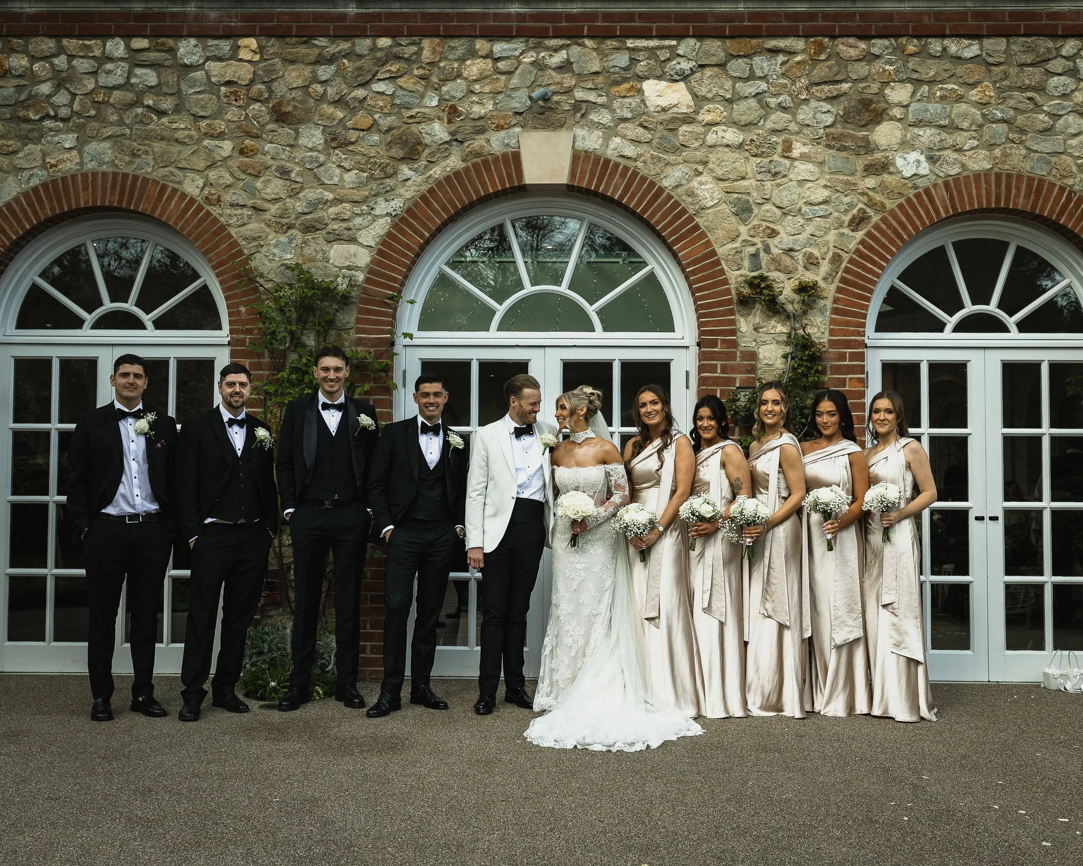 A bridal party in black-tie pose together at the front of The orangery Maidstone.