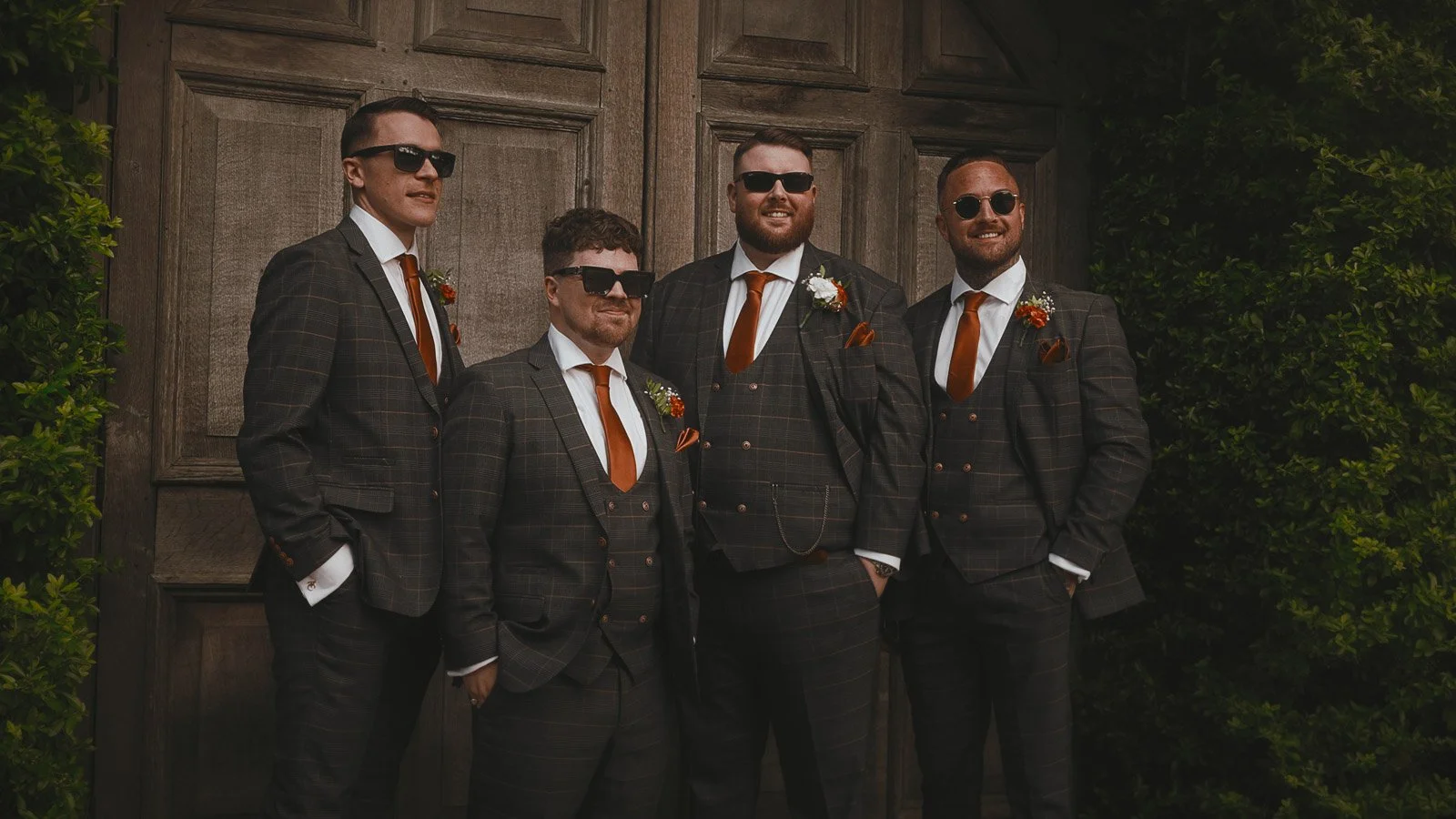 The groom and groomsmen pose for a group shot by the famous wooden barn doors at a colourful outdoor Winters Barns wedding.