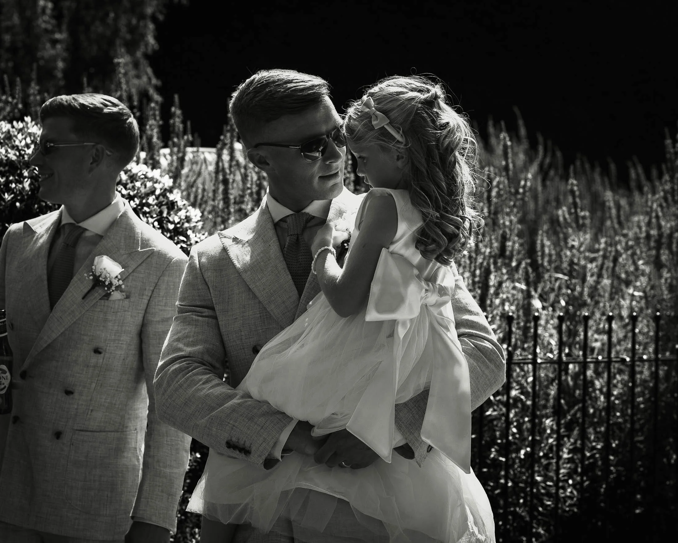 An emotive and authentic wedding photograph showing a groom holding his young daughter in his arms shortly before the outdoor wedding ceremony at Winters Barns in Kent.