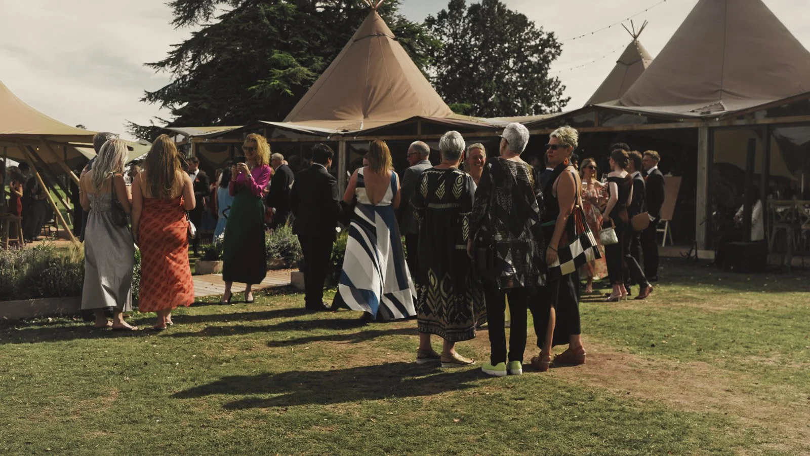 Guests wearing black tie mingle and chat on the terrace at a colourful riverside wedding in the UK.
