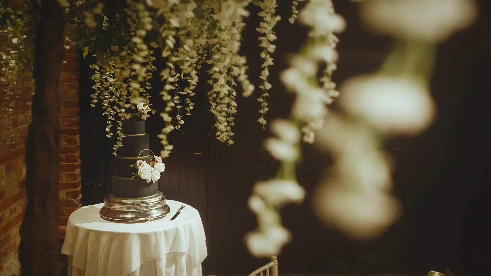 A luxurious 4 tier navy blue wedding cake sits on a plinth in the Tithe Barn at Cooling Castle Barn.