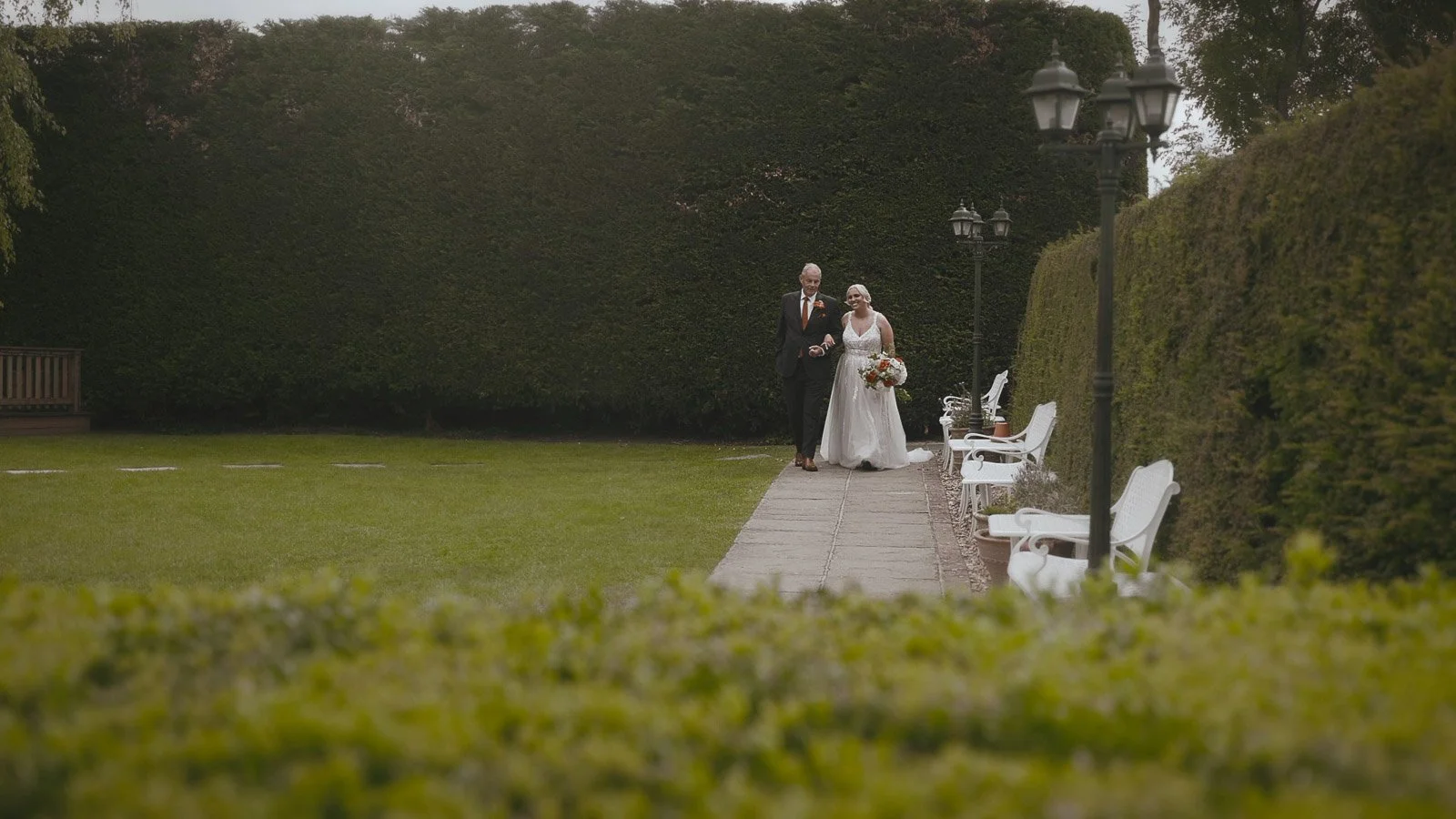 A bride walks with her father down the aisle at a colourful outdoor wedding ceremony at Winters Barns, Canterbury, Kent.