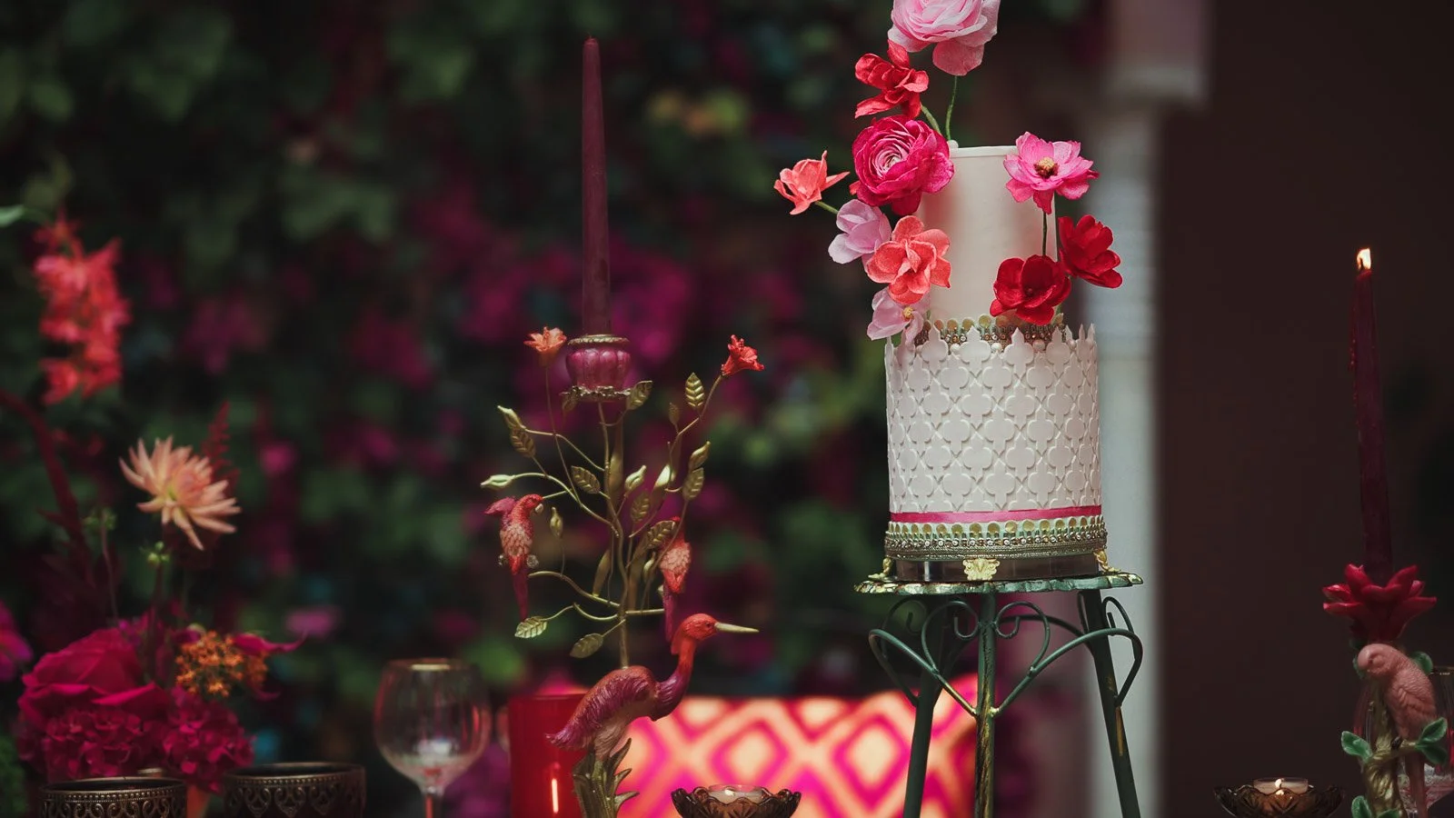 A luxurious and highly detailed wedding cake surrounded by bold pink and red colour palette, framed with and editorial look.