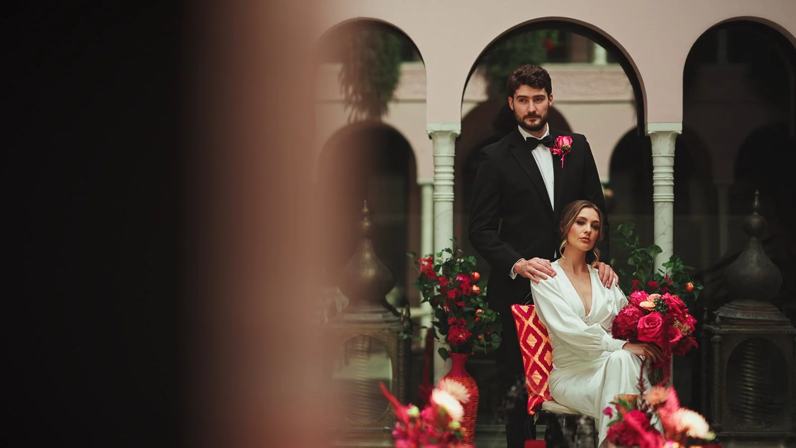 Courtyard scene with bold pink and red florals styled for a colourful fine art wedding aesthetic